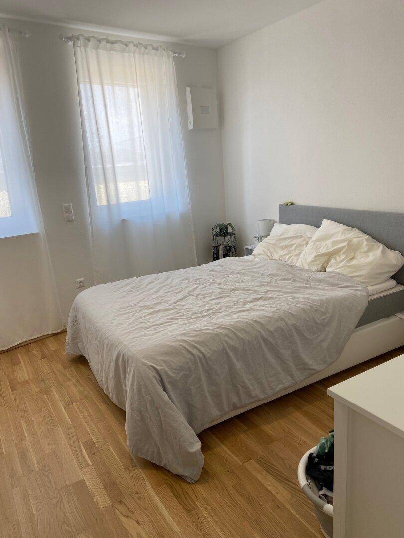 Helles Schlafzimmer mit Doppelbett, Holzboden und großen Fenstern.