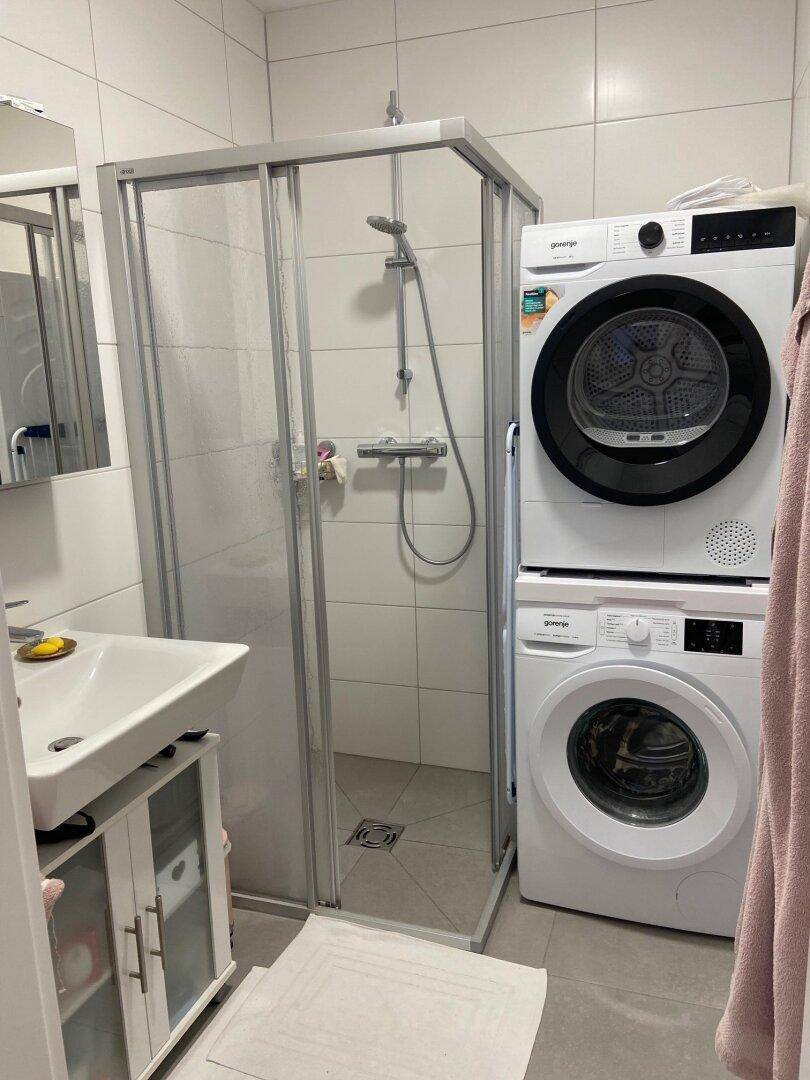 Modernes Badezimmer mit Duschkabine, Waschmaschine und Trockner.