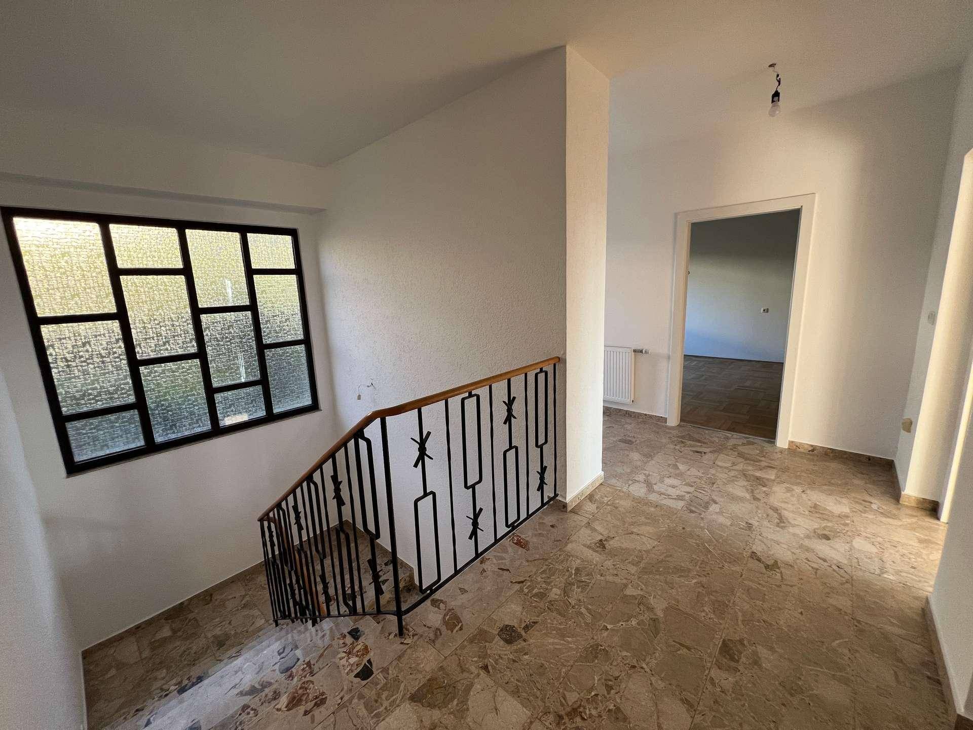 Heller Flur mit Marmorfliesenboden, Treppe mit schmiedeeisernem Geländer und einem dekorativen Fenster.