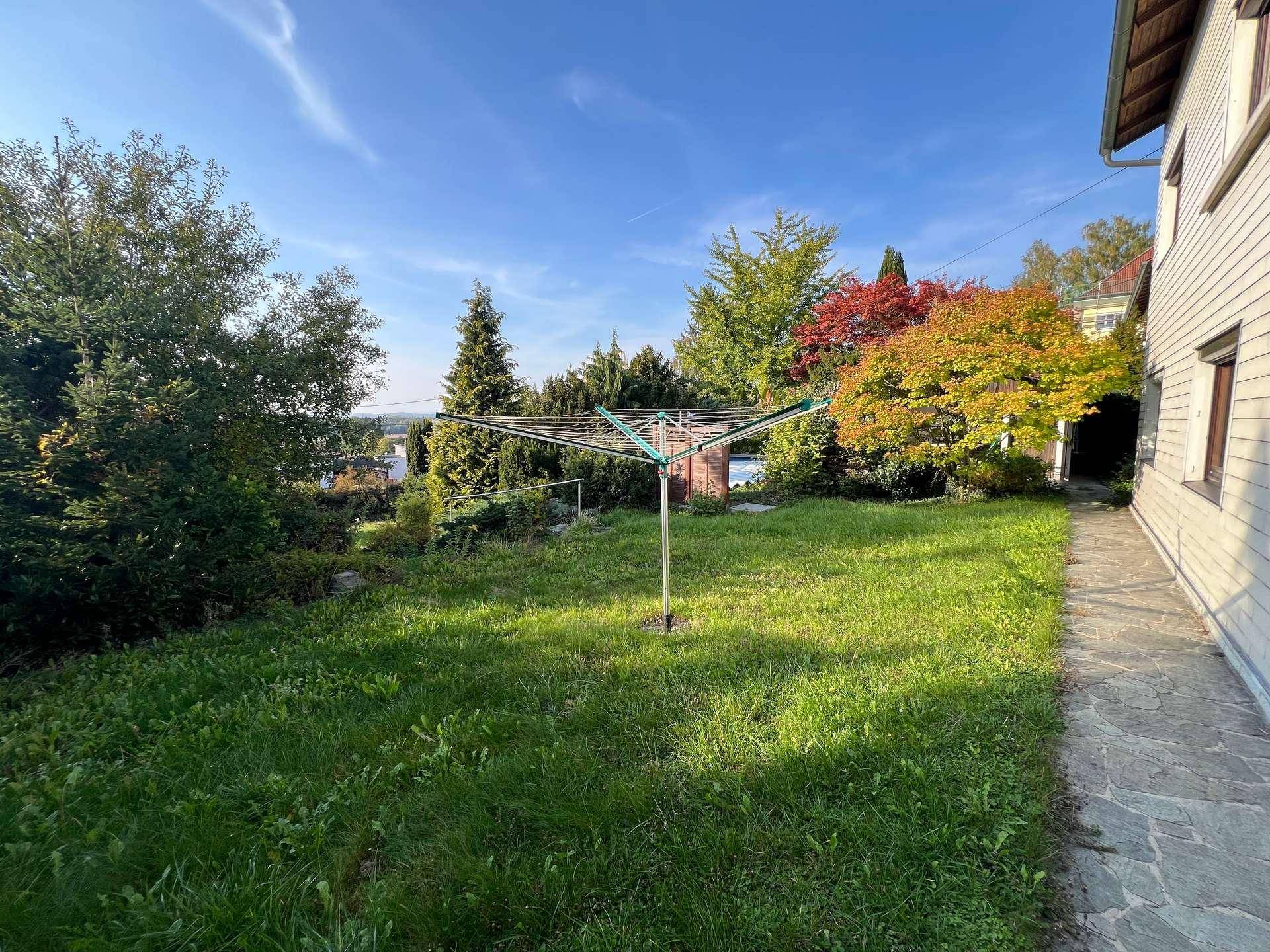Gepflegter Gartenbereich mit Wäschespinne, Rasenfläche und vielfältiger Bepflanzung unter blauem Himmel.