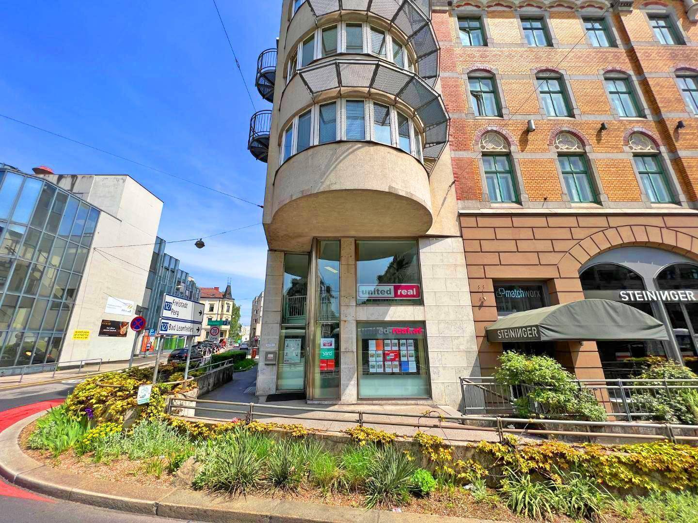 Außenansicht eines modernen Geschäftsgebäudes mit markanter Architektur und großen Schaufenstern an einer belebten Straße.