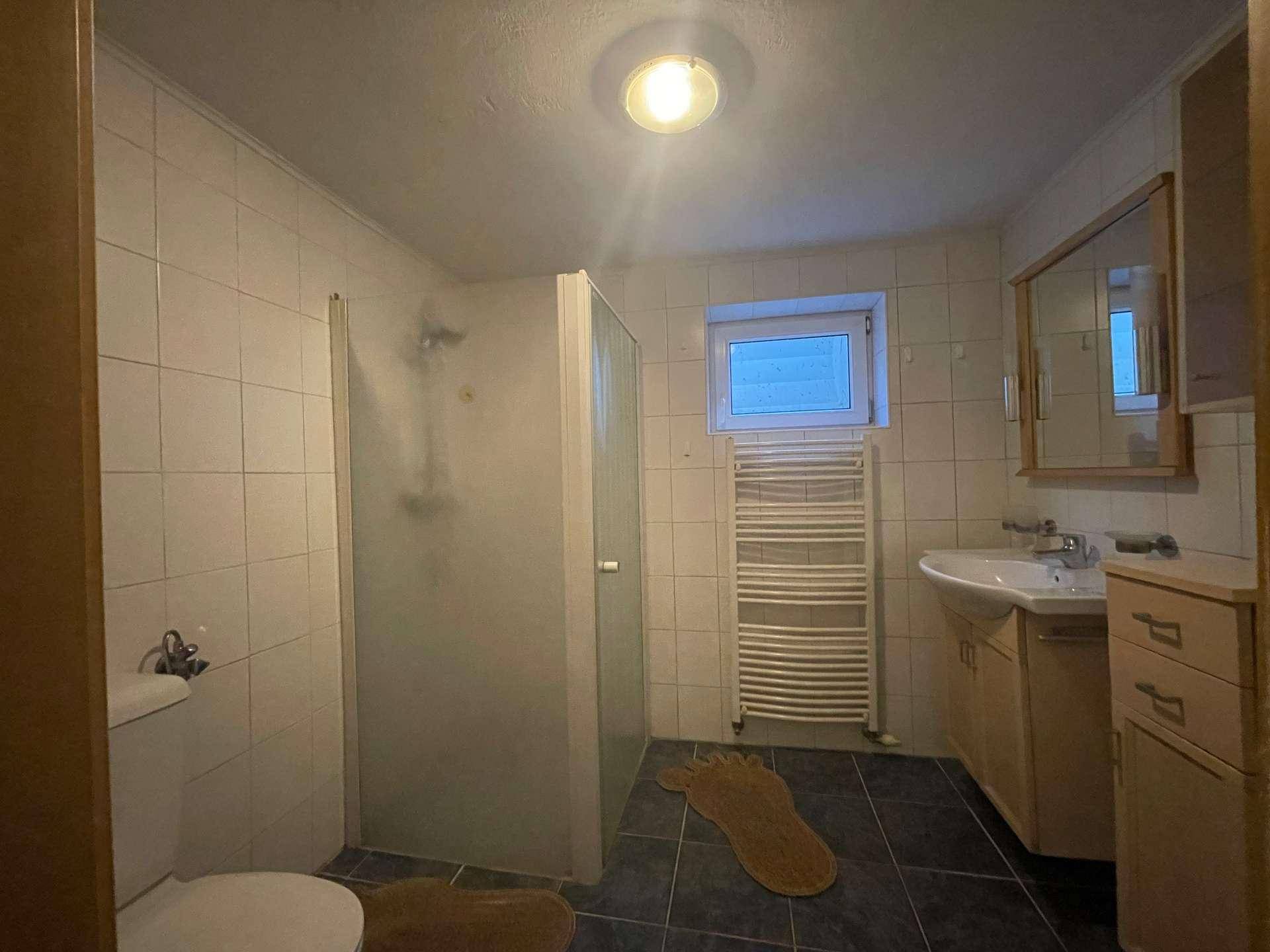 Funktionales Badezimmer mit Dusche, Waschbecken, WC, Fenster und beheiztem Handtuchhalter.