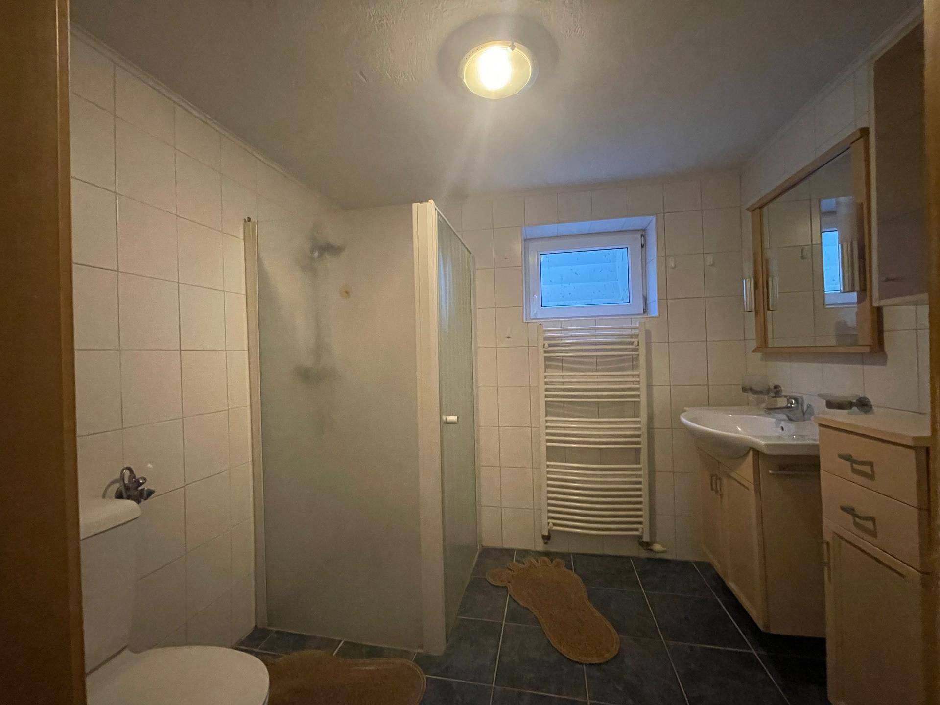Badezimmer mit Duschkabine, Waschbecken und beheiztem Handtuchhalter, gefliest in Weiß und Dunkelblau.