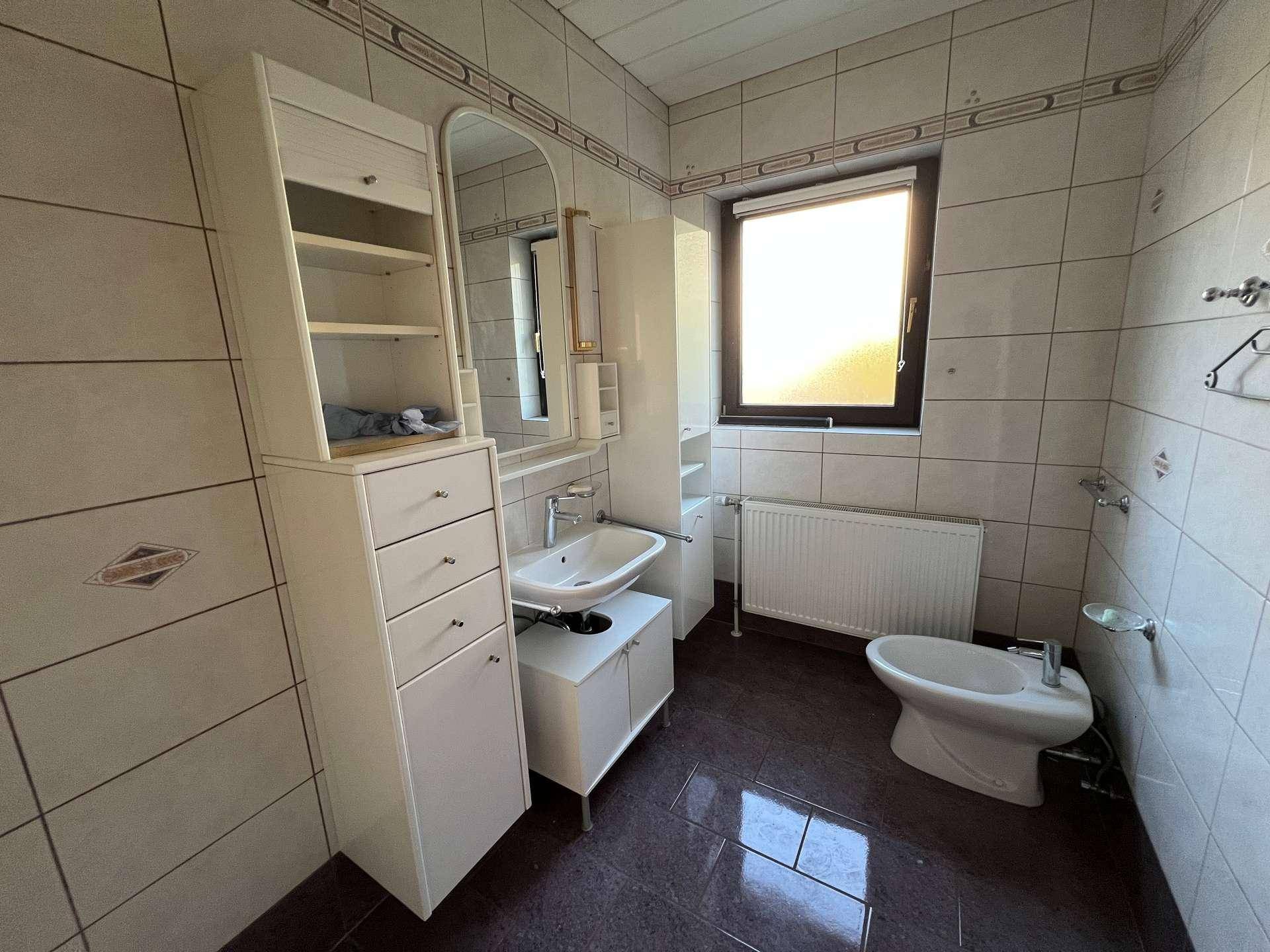 Helles Badezimmer mit Fliesen, Einzelwaschbecken, Spiegelschrank, Bidet und einem Fenster.