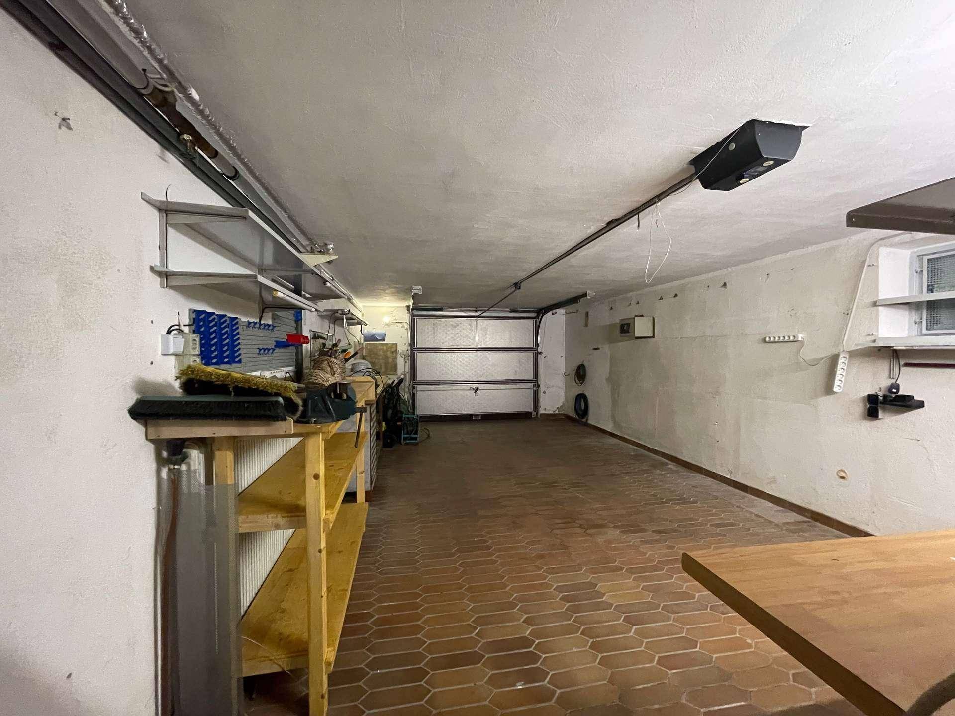 Geräumige Garage mit Terrakotta-Fliesenboden, Werkbank und viel Stauraum.