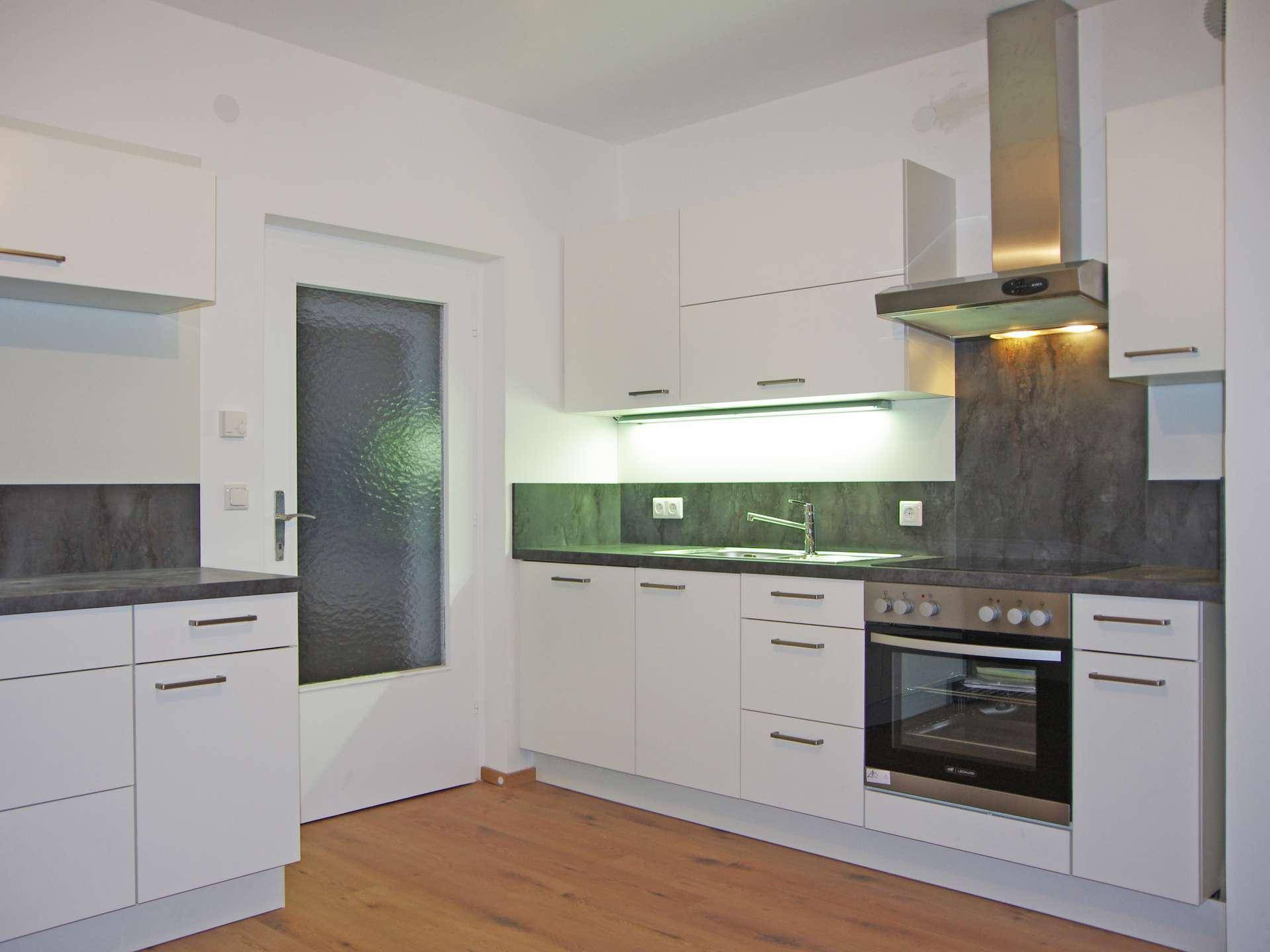 Moderne Küche mit weißen Schränken, dunklen Arbeitsplatten und Edelstahlofen.