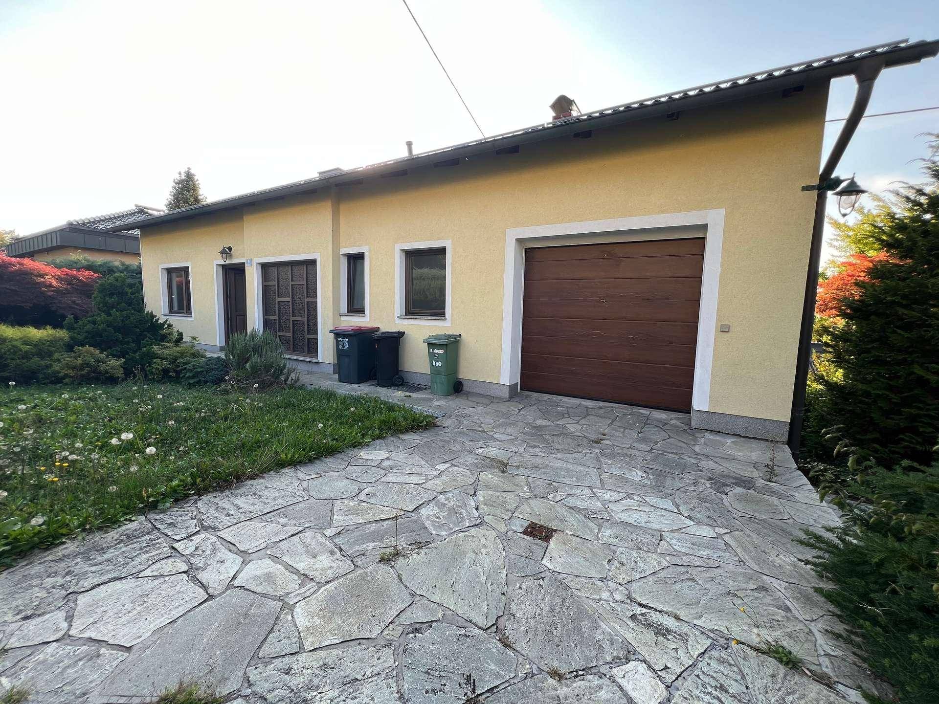 Einfamilienhaus mit integrierter Garage, gepflasterter Auffahrt und kleinem Vorgarten.