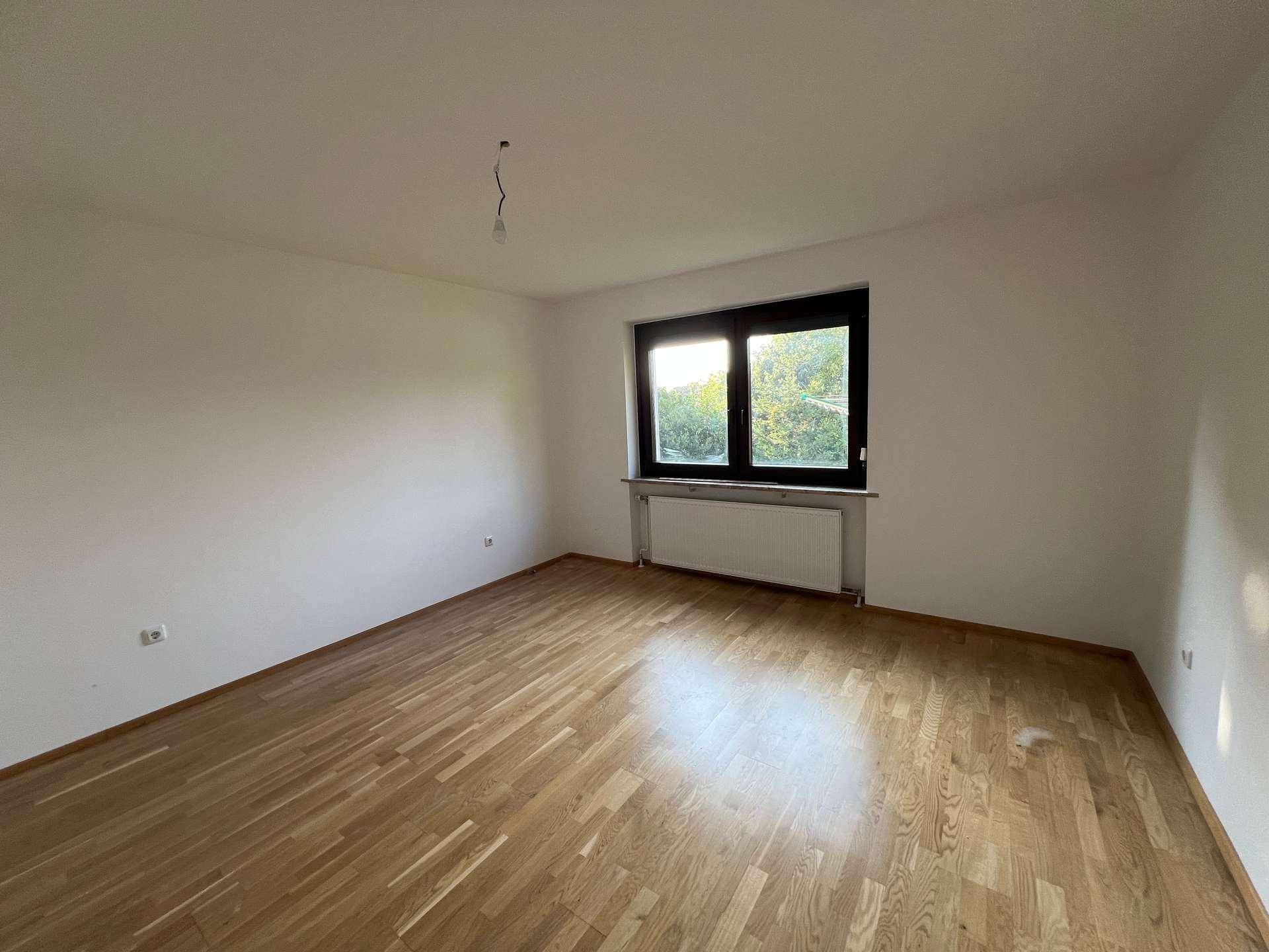 Geräumiges Schlafzimmer mit Parkettboden und einem großen Fenster, das viel Tageslicht hereinlässt.