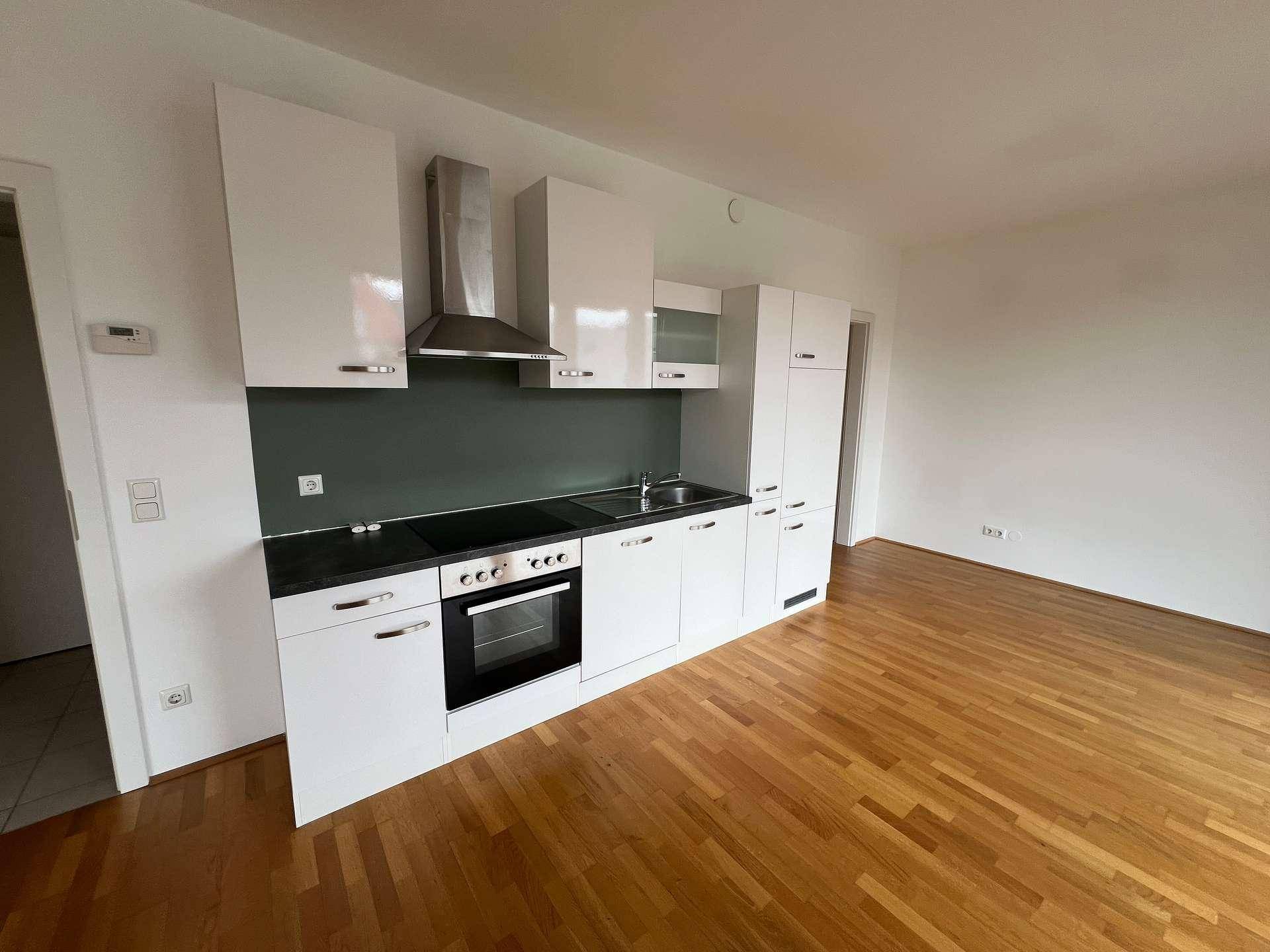 Funktionale Einbauküche mit weißen Fronten, Kochfeld, Backofen und Dunstabzugshaube, ideal für offenes Wohnen.
