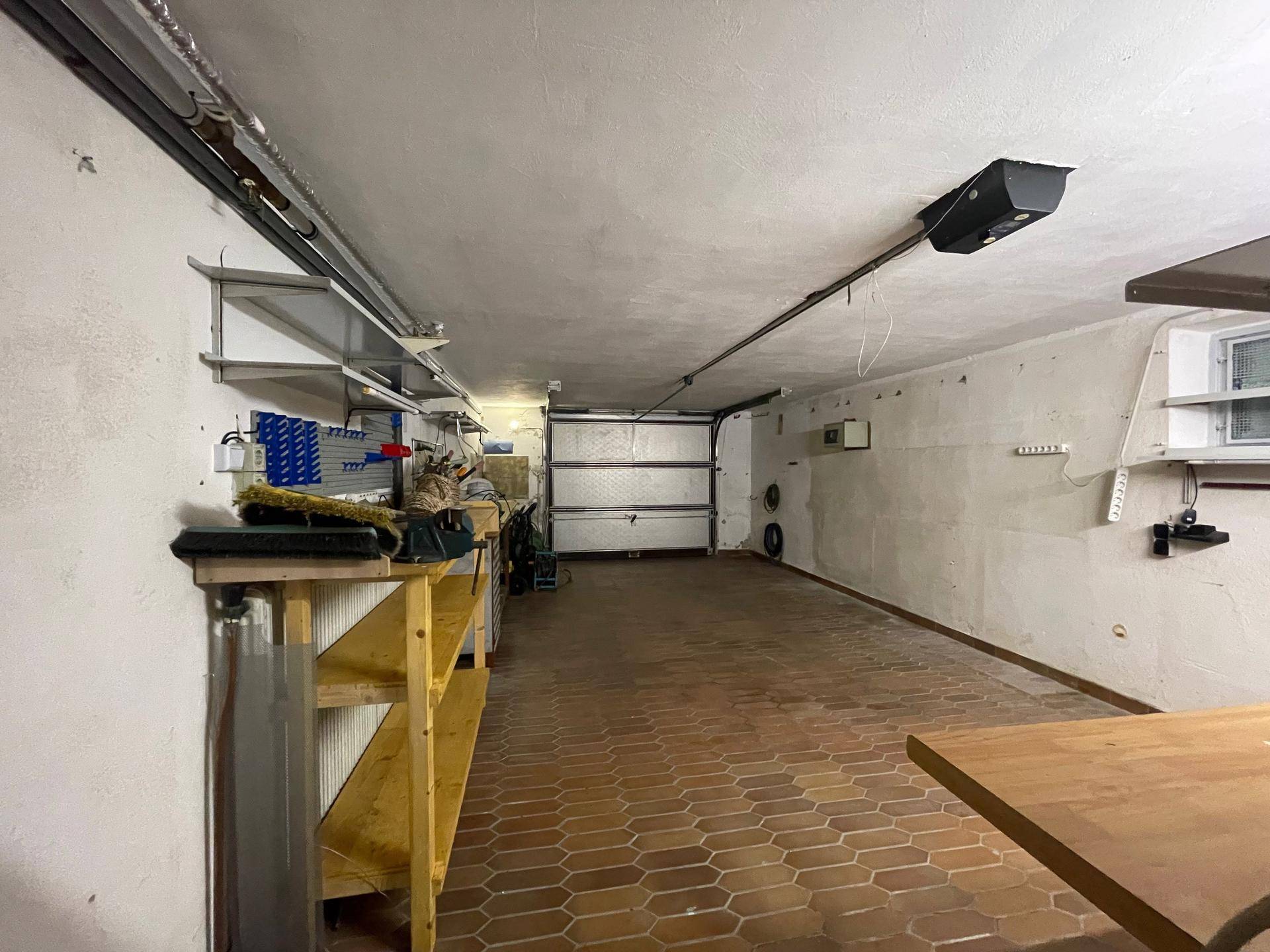 Geräumige Garage mit Fliesenboden, Werkstattbereich und automatischem Garagentor.