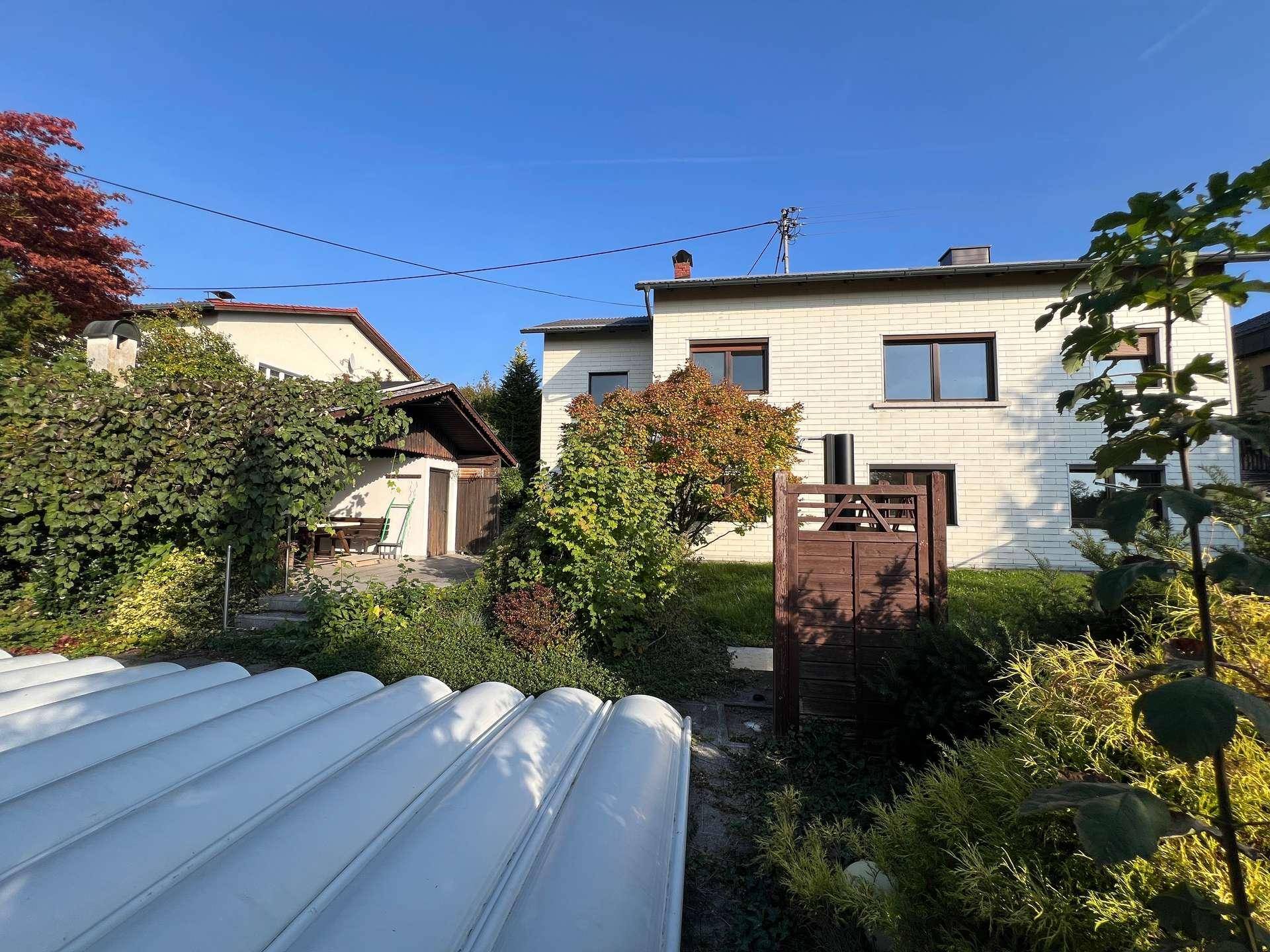Rückansicht eines Hauses mit weißer Ziegelfassade und Gartenbereich mit abgedecktem Pool.