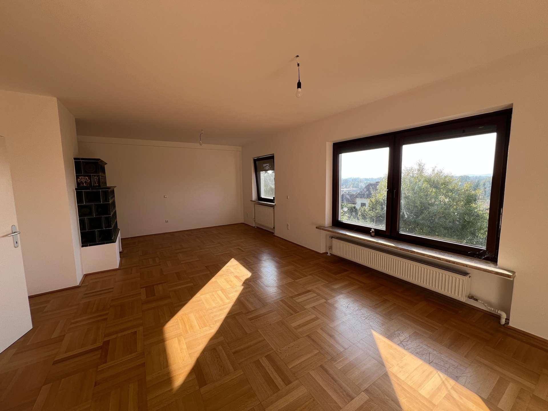 Helles Wohnzimmer mit Parkettboden, großen Fenstern und einem traditionellen Kachelofen in der Ecke.