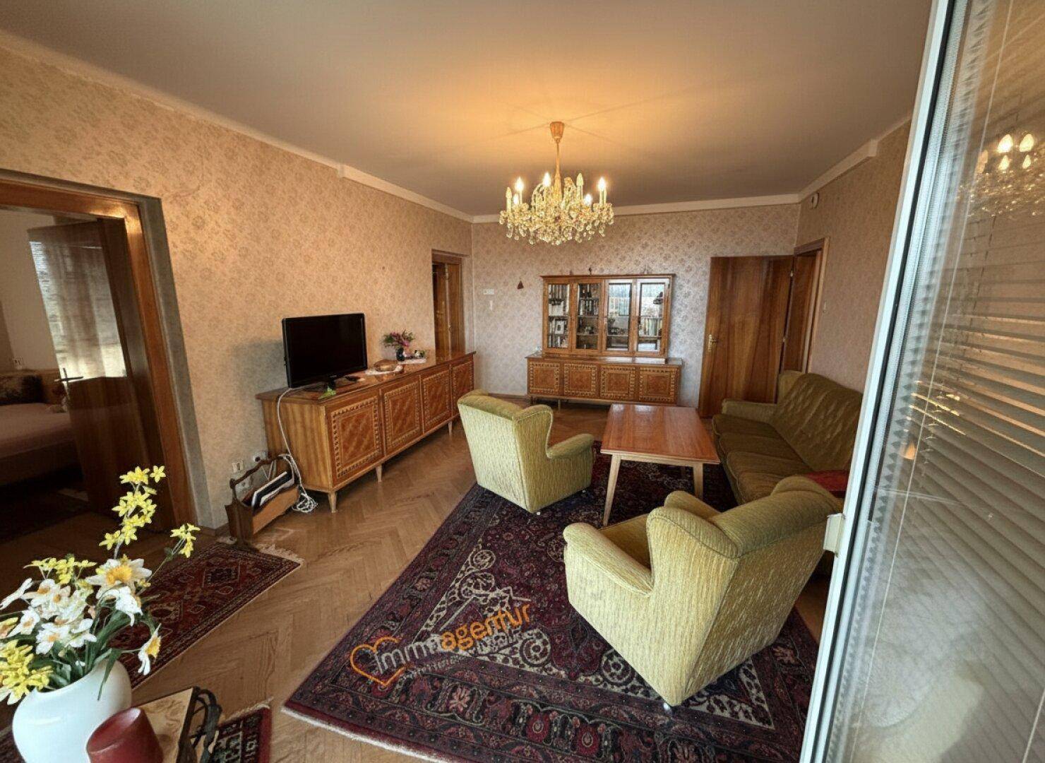 Gemütliches Wohnzimmer mit traditionellen Möbeln, gemusterter Tapete und einem Kronleuchter.