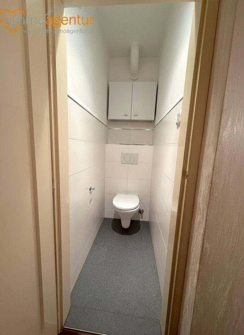 Separates WC mit wandhängender Toilette und weißen Fliesen an den Wänden.