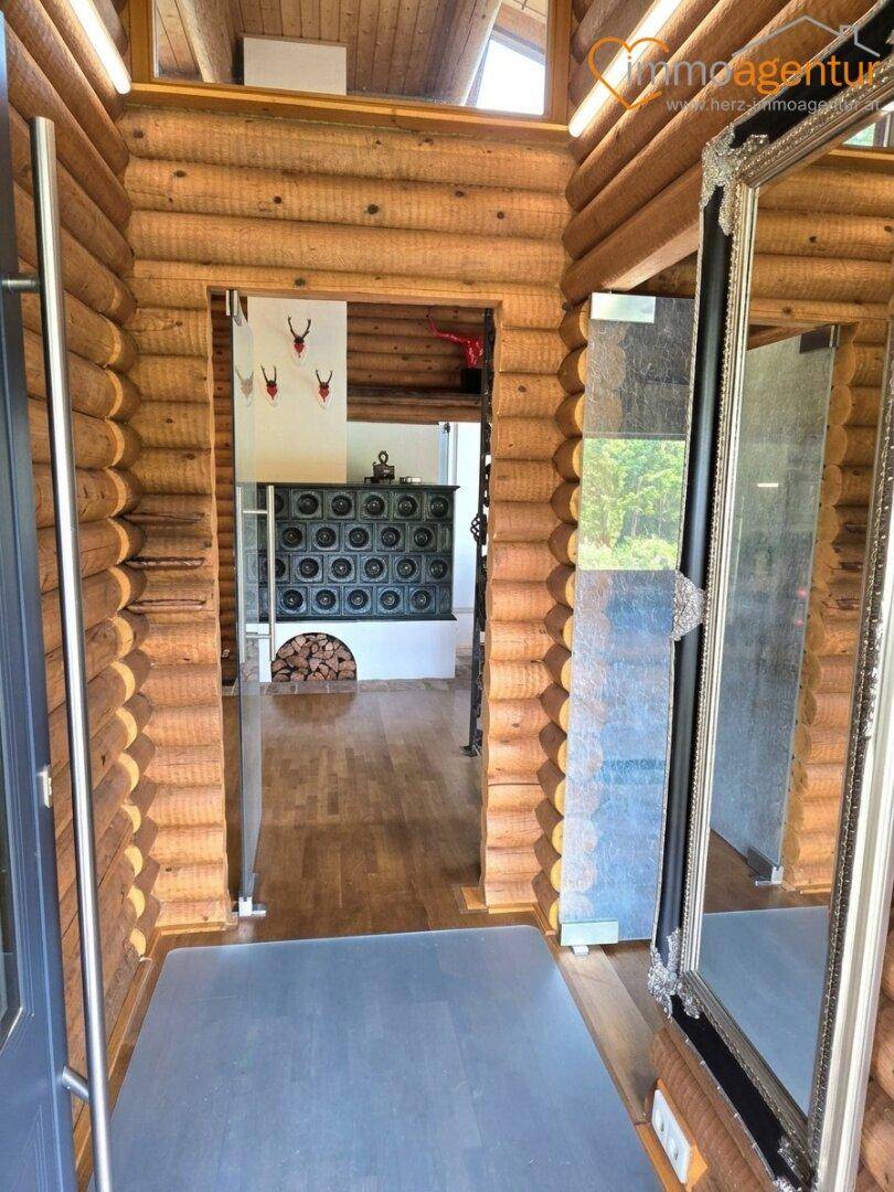 Rustikaler Eingangsbereich im Blockhaus mit Holzwänden und Blick auf den traditionellen Kachelofen.