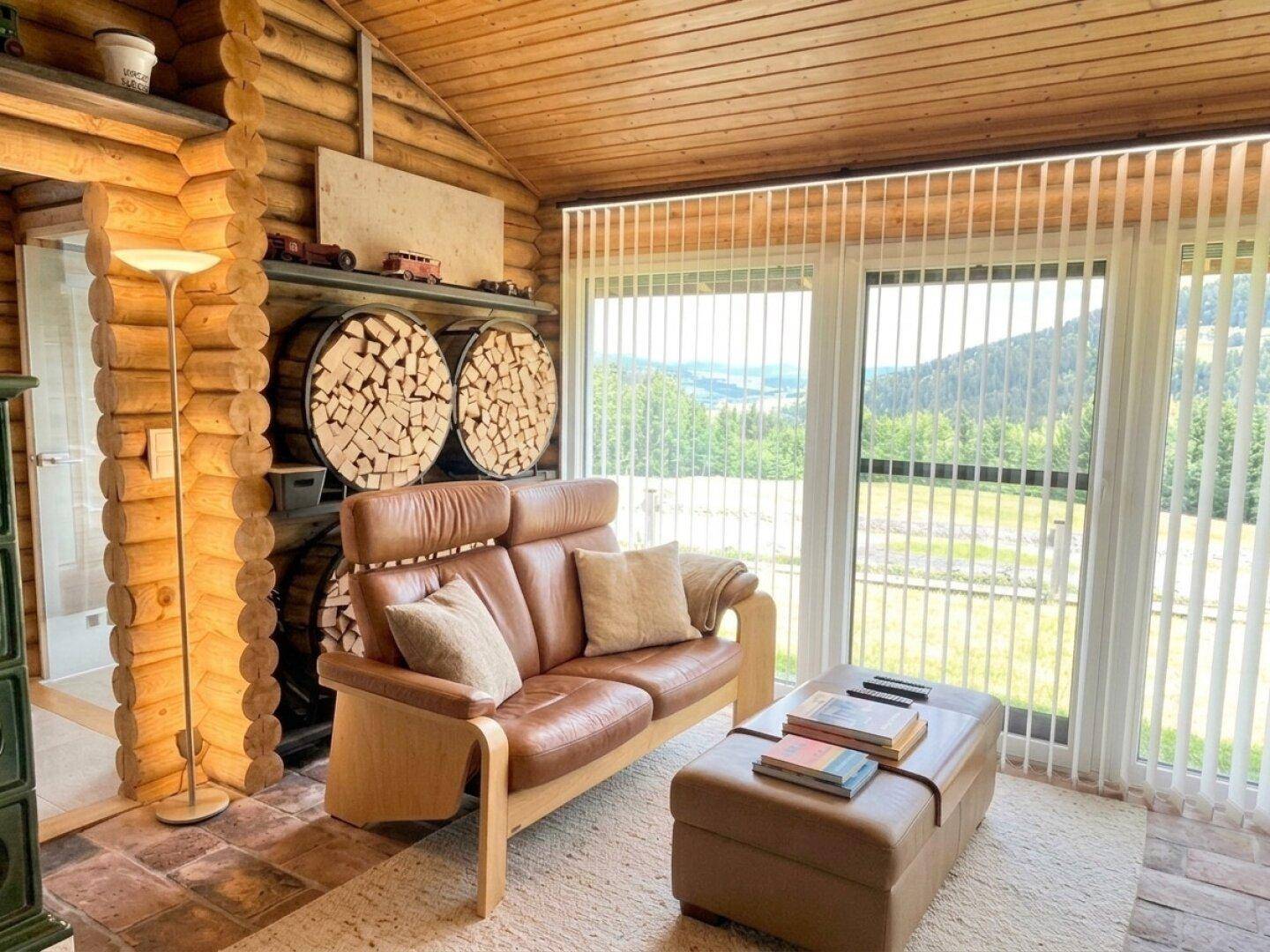 Gemütlicher Wohnbereich mit Ledersofa, Holzwänden und großen Fenstern mit weitem Ausblick.