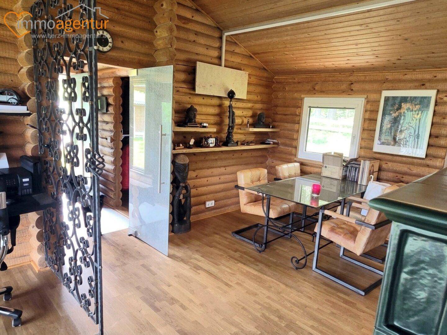 Helles Arbeitszimmer im Blockhaus mit Holzböden, Glastisch und dekorativem schmiedeeisernem Element.