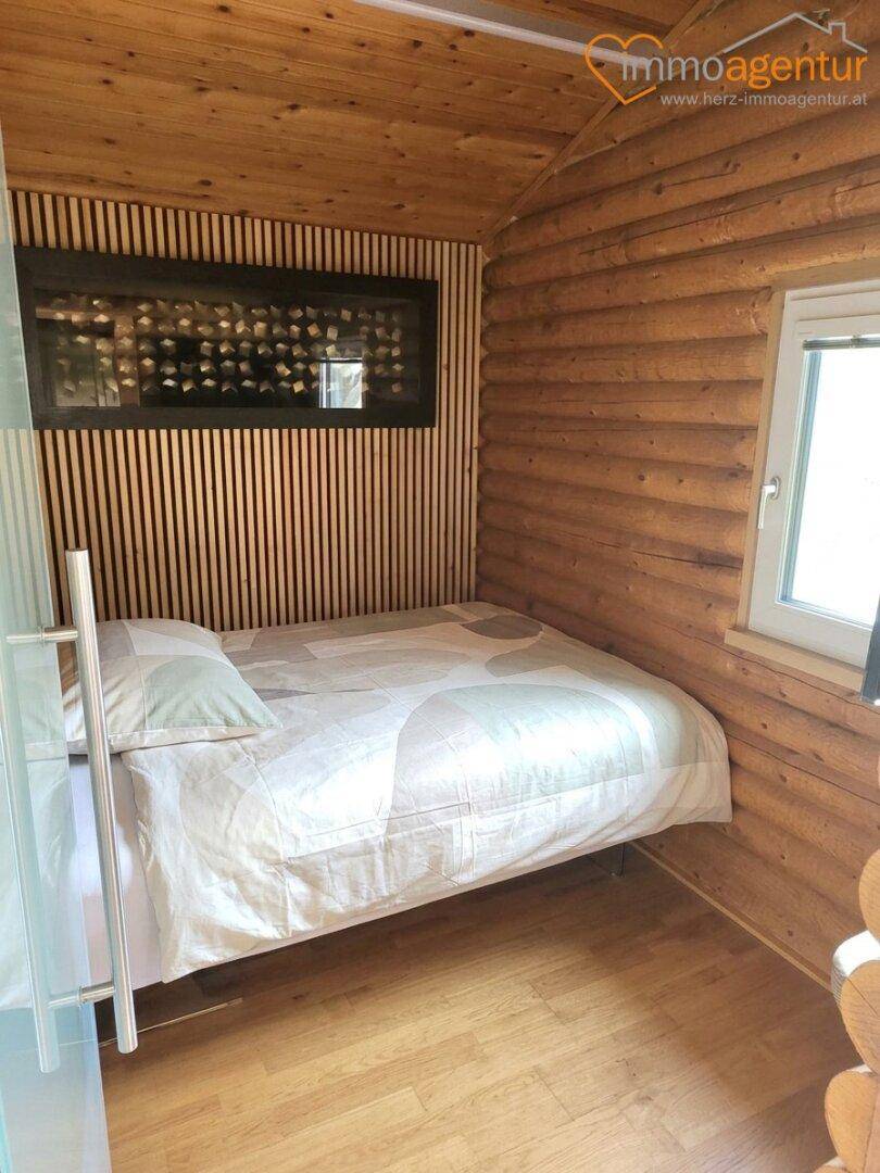 Gemütliches Schlafzimmer im Blockhausstil mit Holzwänden, Einzelbett und integriertem Weinregal.
