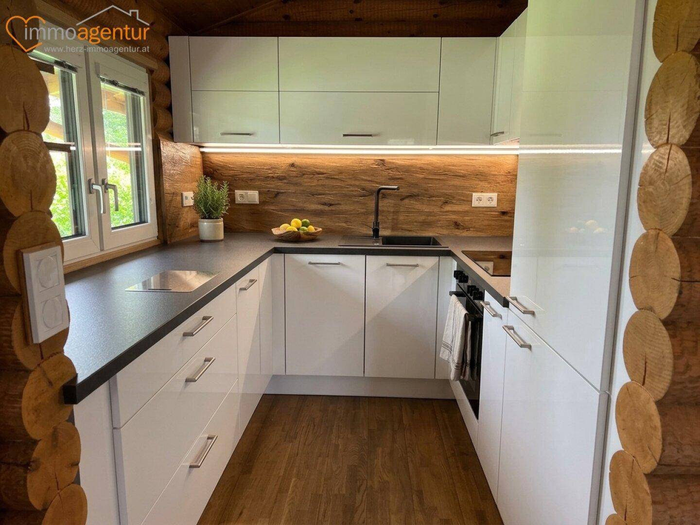 Moderne weiße Einbauküche mit dunkler Arbeitsplatte und Holzwänden im Blockhausstil.