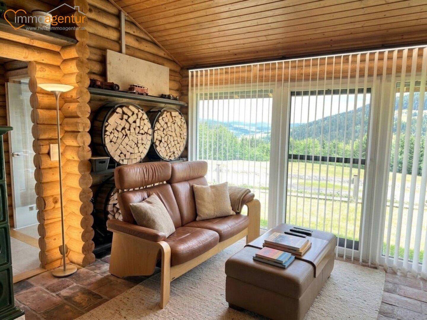 Gemütlicher Wohnbereich mit Ledersofa, Holzwänden und großen Fenstern mit weitem Ausblick.