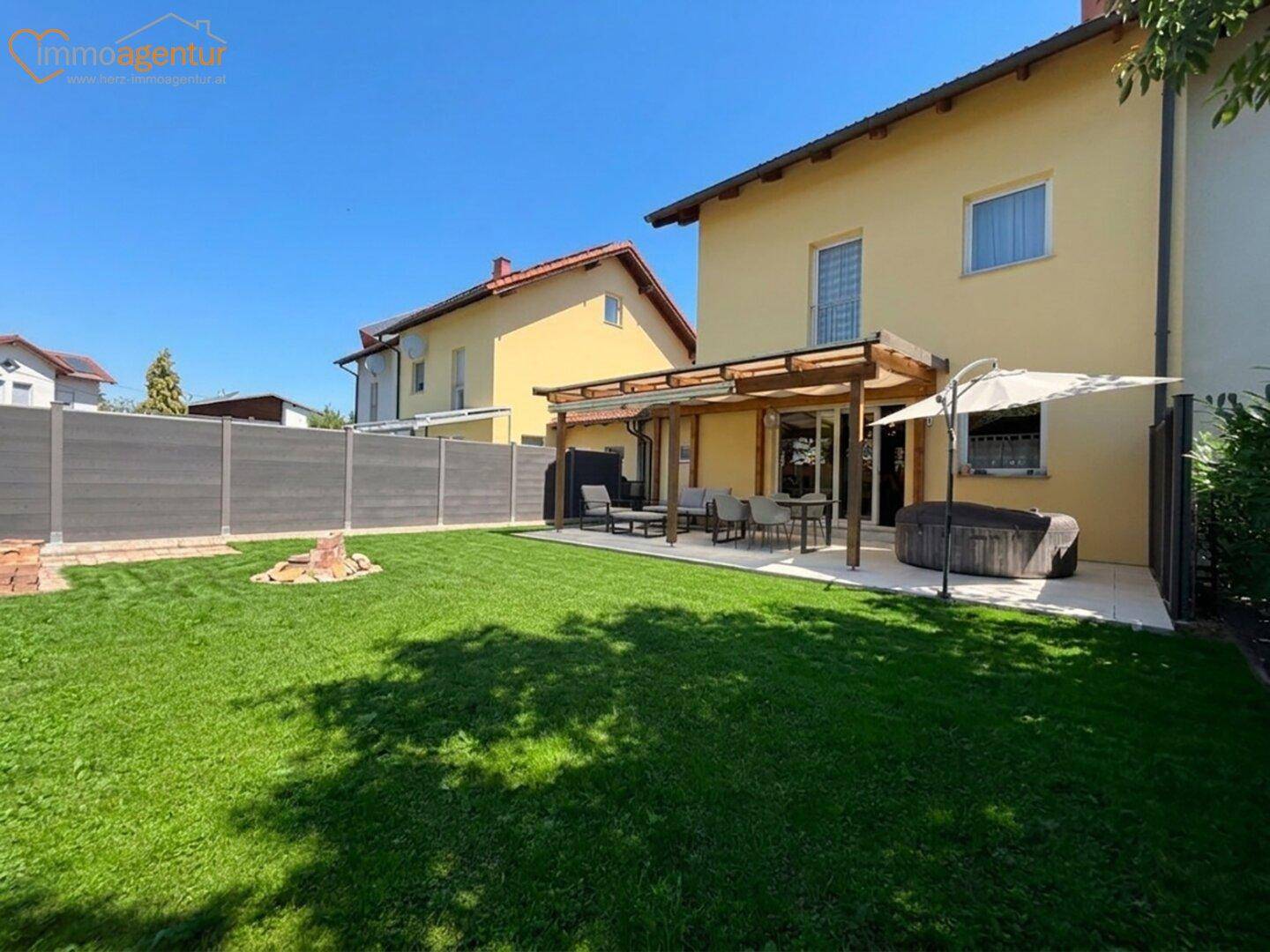 Gepflegter Garten mit Rasenfläche, überdachter Terrasse und Sitzgelegenheiten im Freien.