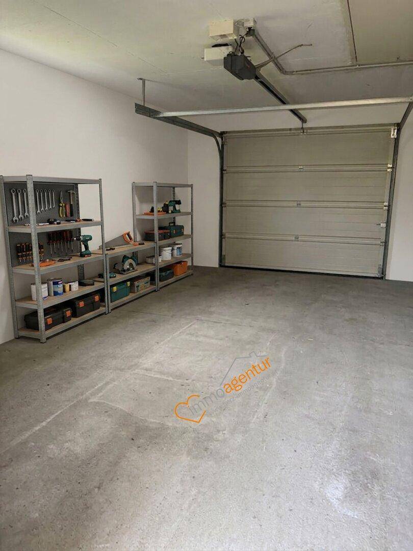 Geräumige Garage mit Betonboden, Werkzeugregalen und automatischem Garagentor.