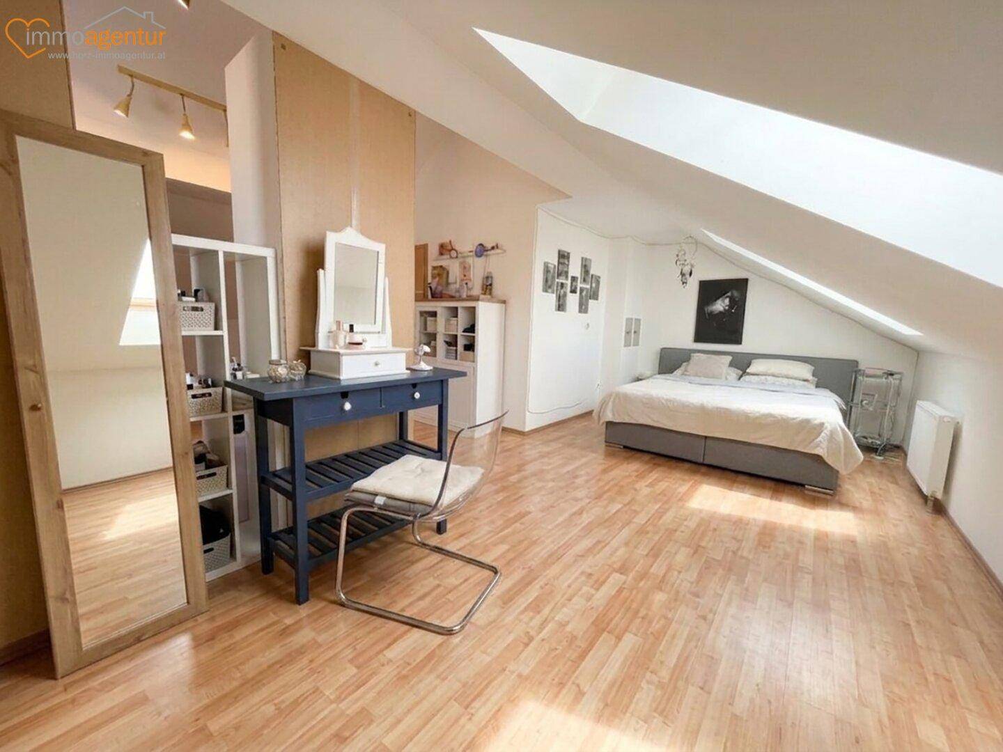 Großes Schlafzimmer im Dachgeschoss mit Holzboden, Schminktisch und Dachfenstern.