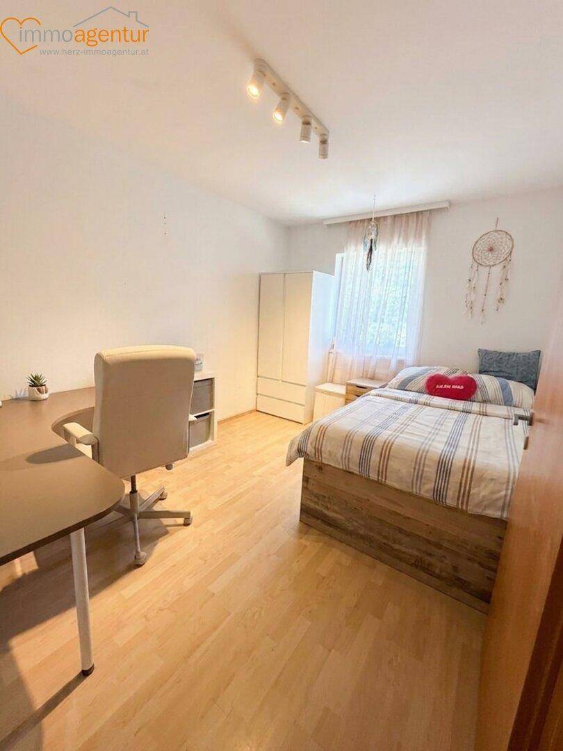 Helles Schlafzimmer mit Holzboden, Bett, Schreibtisch und Fenster.