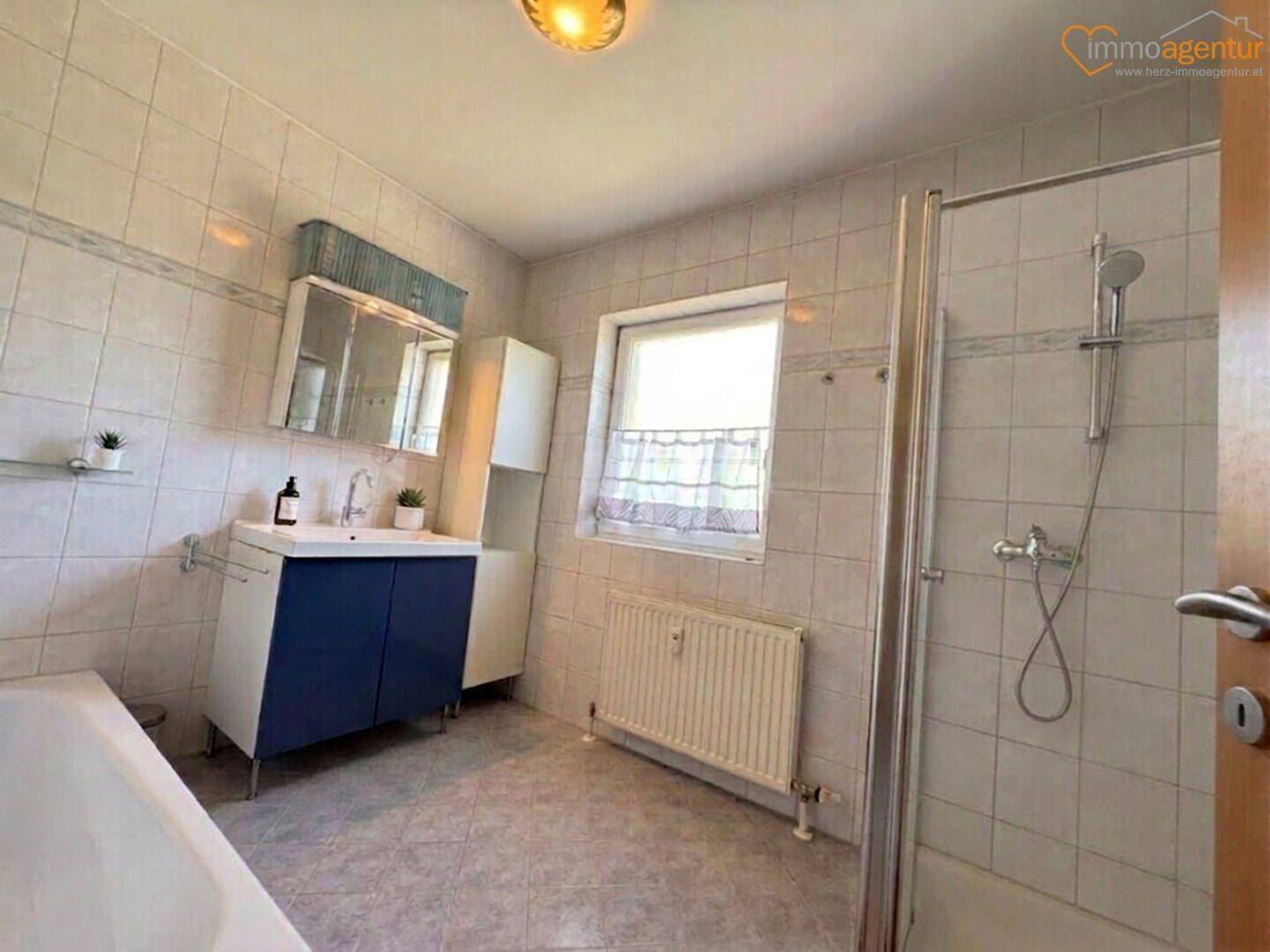 Gefliestes Badezimmer mit Dusche, Badewanne, Einzelwaschbecken und Fenster.
