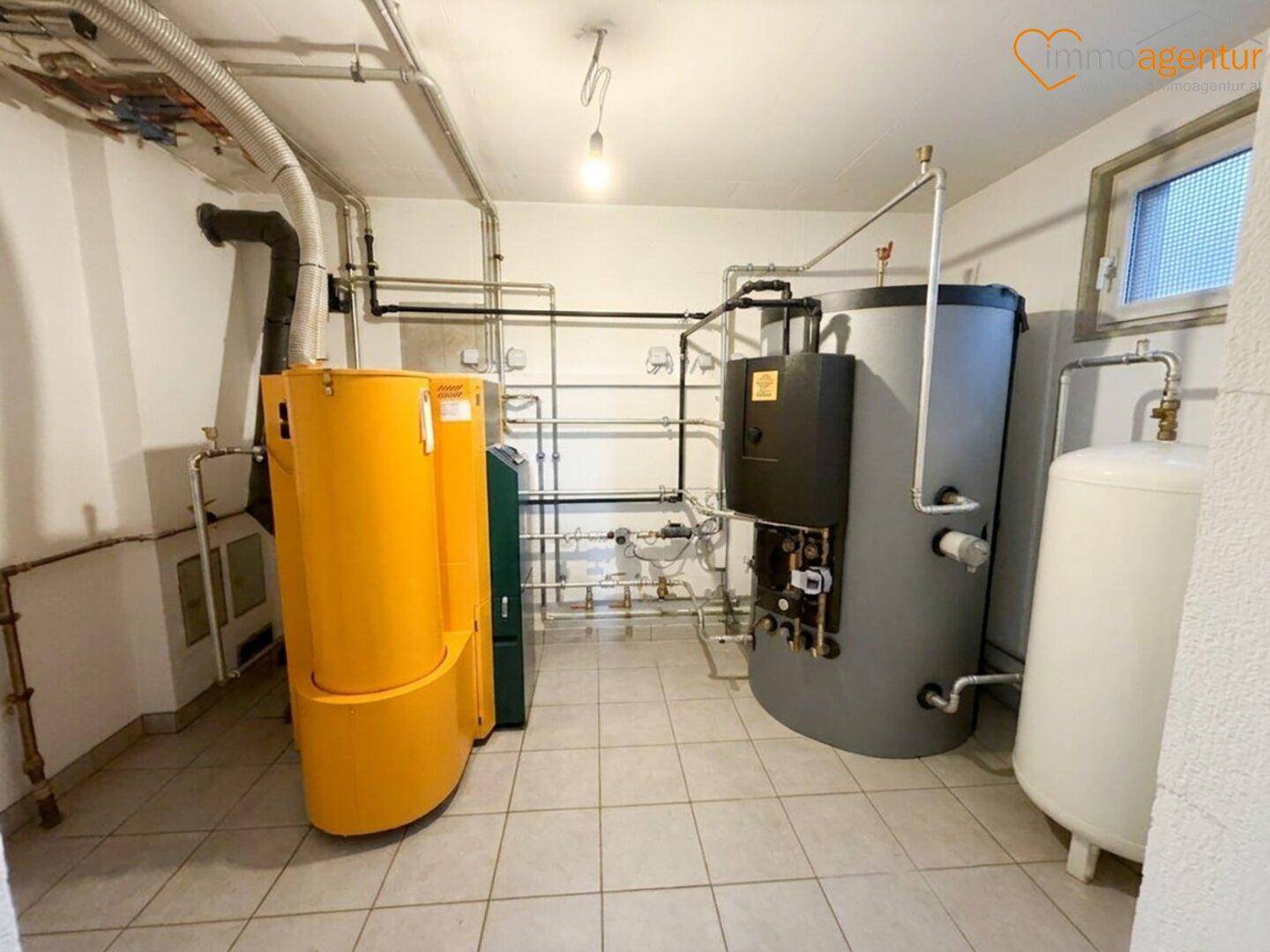 Technikraum im Keller mit Heizungsanlage, Warmwasserspeicher und Fliesenboden.