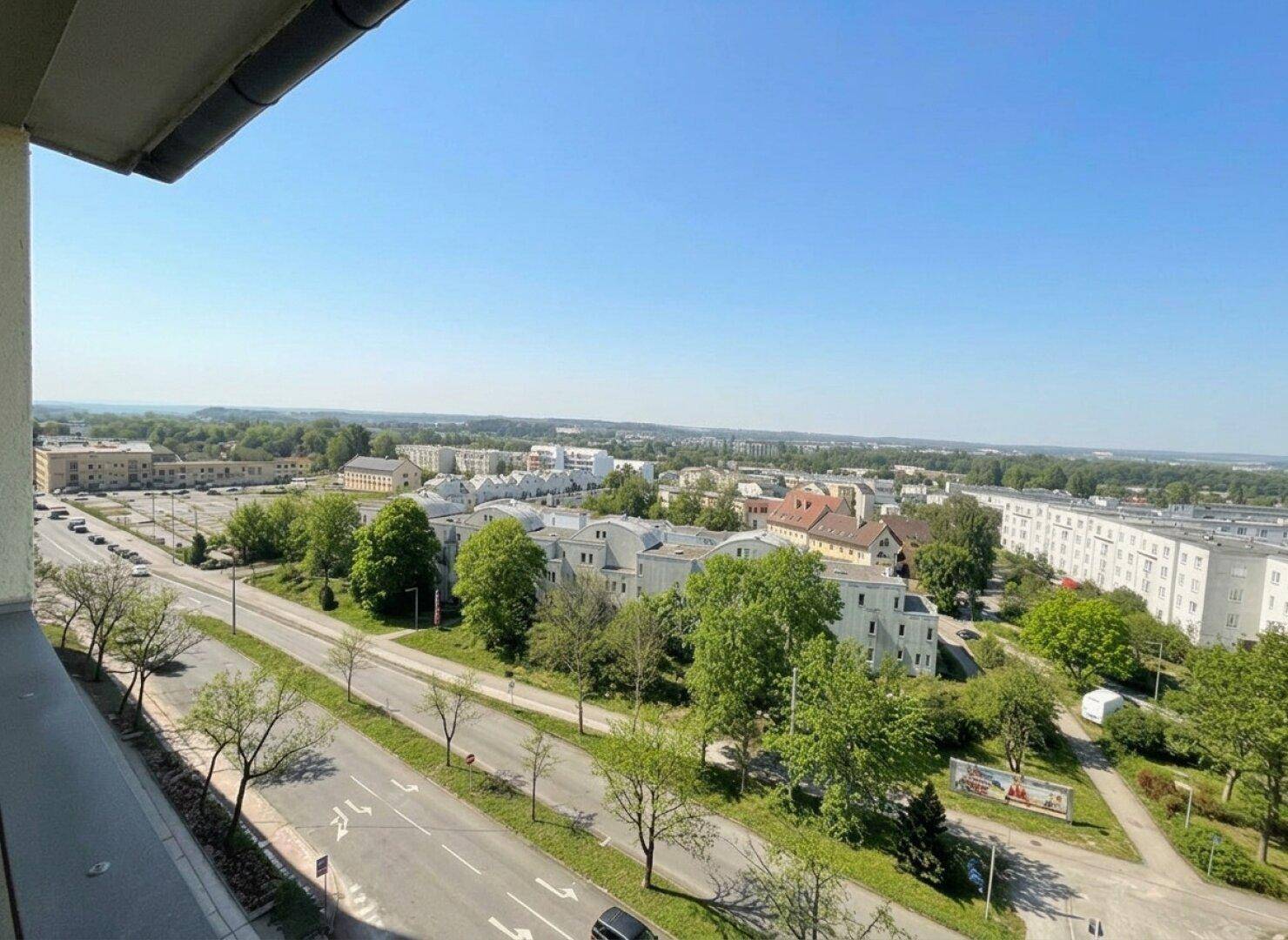 Panoramablick über eine grüne Stadtlandschaft mit vielen Bäumen und Gebäuden an einem sonnigen Tag.