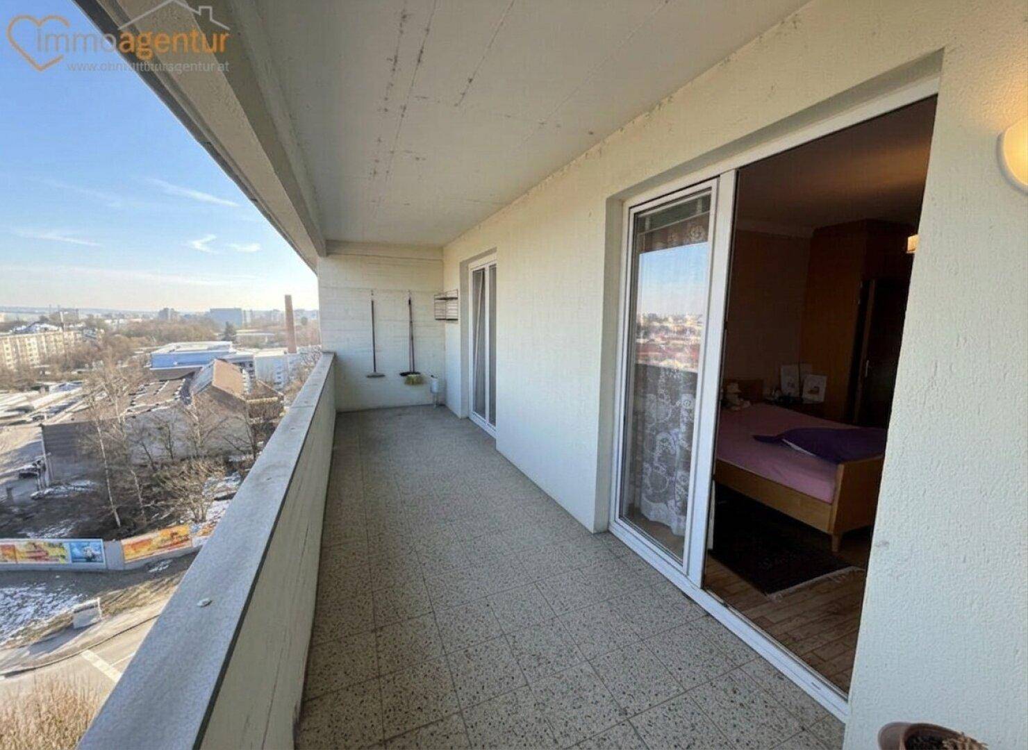 Geräumiger Balkon mit Fliesenboden und Zugang zu einem Schlafzimmer, bietet einen weiten Stadtblick.