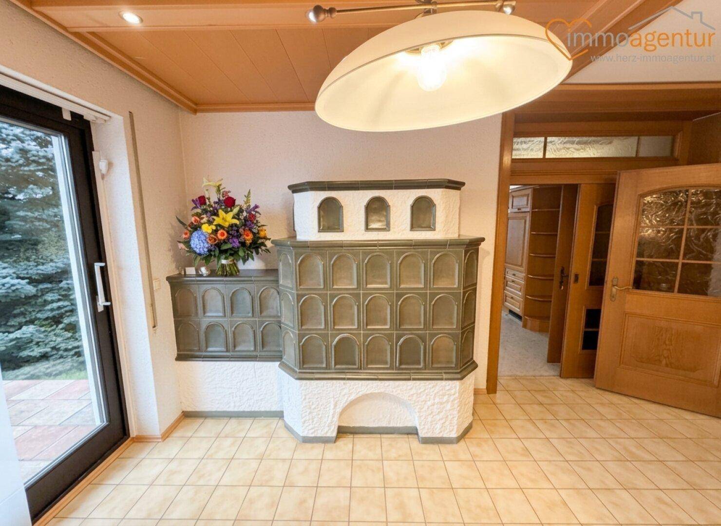 Traditioneller Kachelofen als zentrales Element in einem gefliesten Raum mit Holztür.