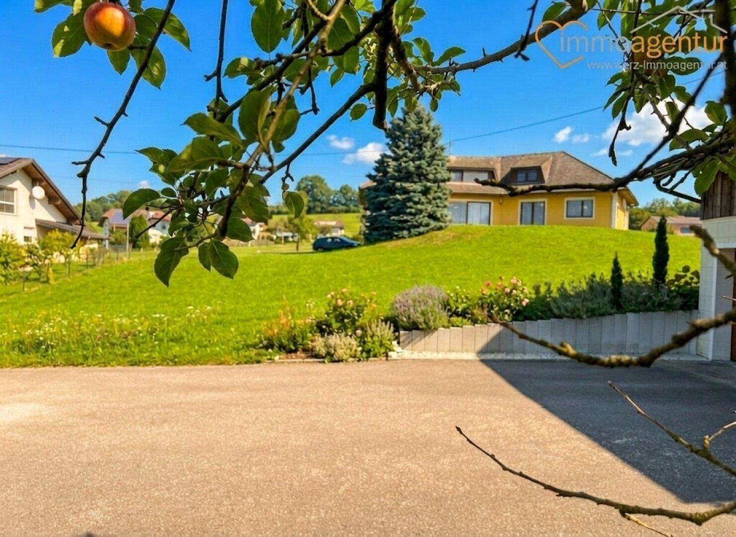 Das Haus liegt eingebettet in eine grüne Hügellandschaft mit Obstbäumen und weitem Blick.