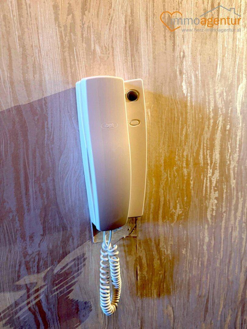 Gegensprechanlage an einer holzverkleideten Wand im Eingangsbereich.