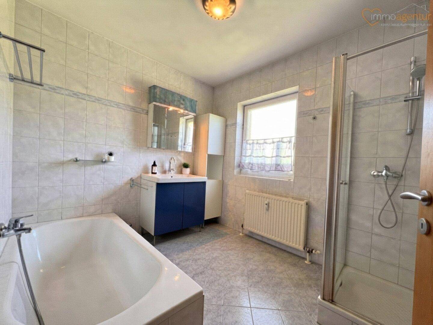 Gefliestes Badezimmer mit Badewanne, Duschkabine, Einzelwaschbecken und Fenster.
