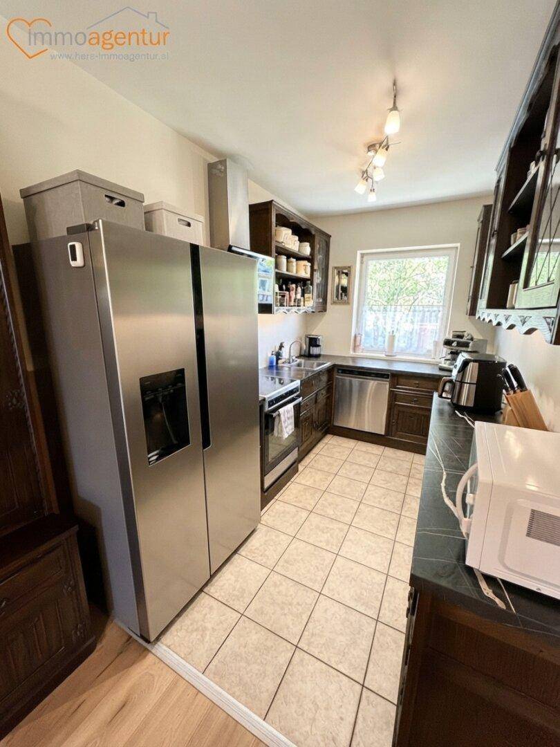Funktionale Küche mit dunklen Holzschränken, Fliesenboden, großem Kühlschrank und Fenster.