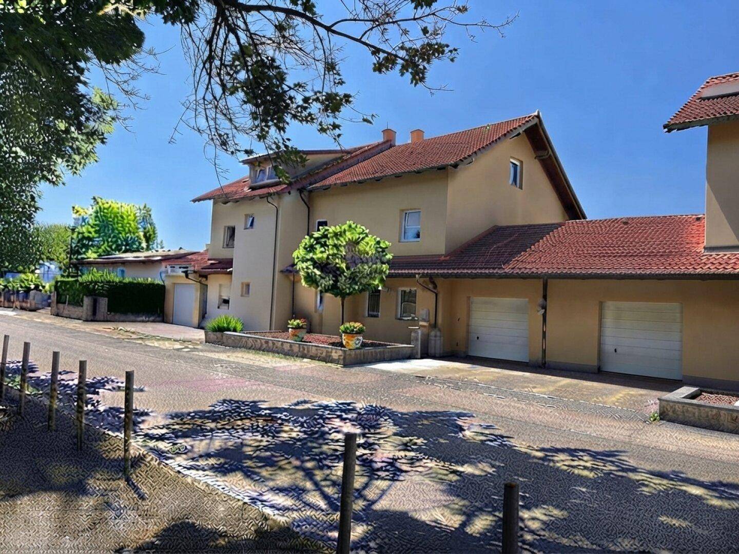 Ansicht des Hauses von der Straße mit Garagen und gepflegter Außenanlage unter blauem Himmel.