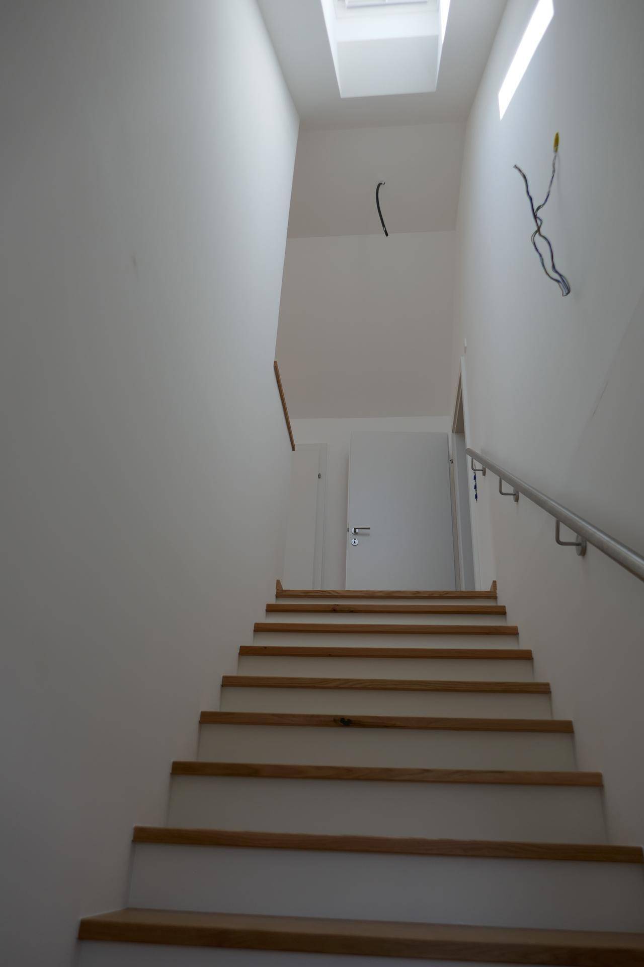 Helles Treppenhaus mit Holzstufen, weiß gestrichenen Wänden und einem Oberlicht für natürliche Beleuchtung.