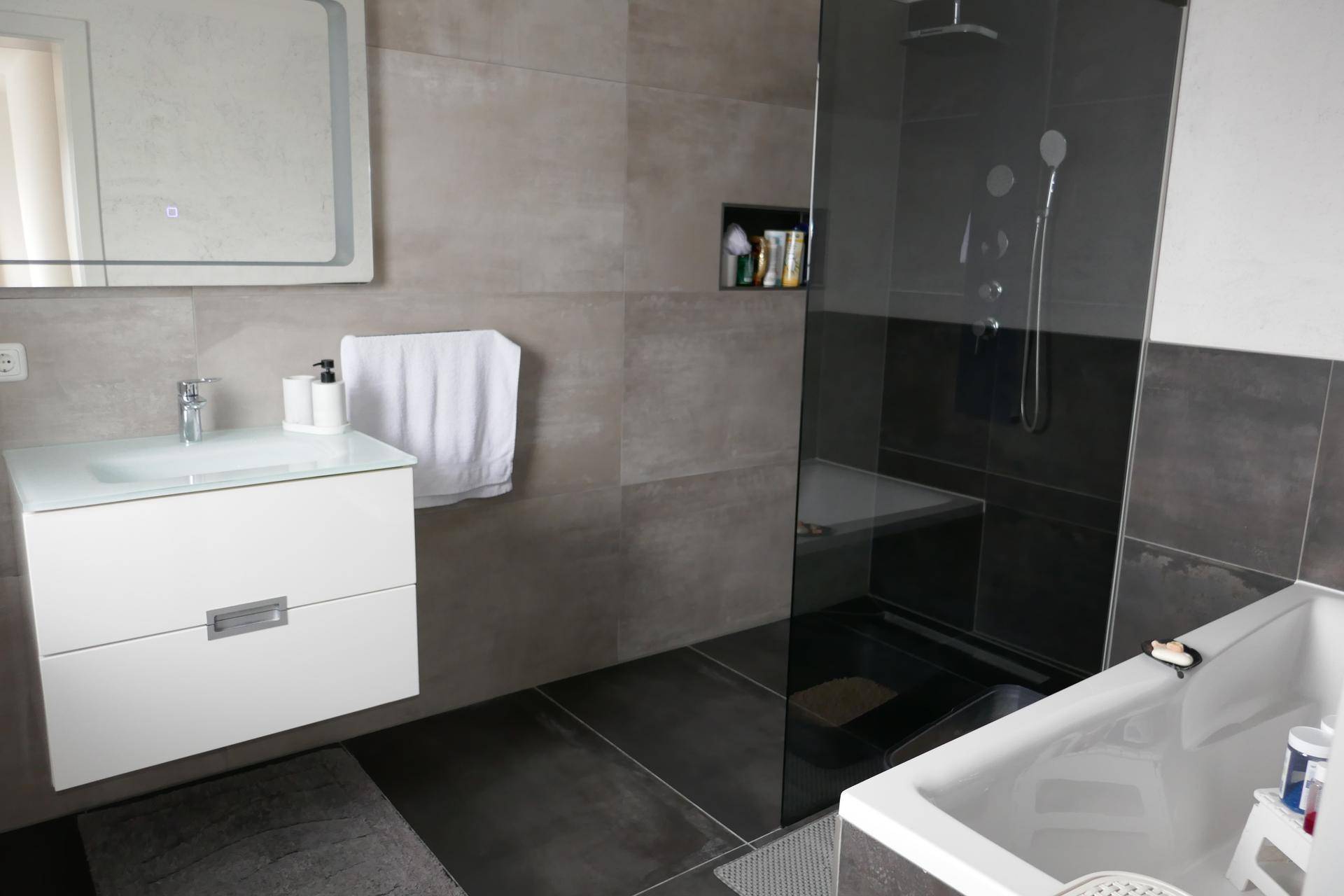 Elegantes Badezimmer mit grauen Großformatfliesen, moderner Dusche und Badewanne.