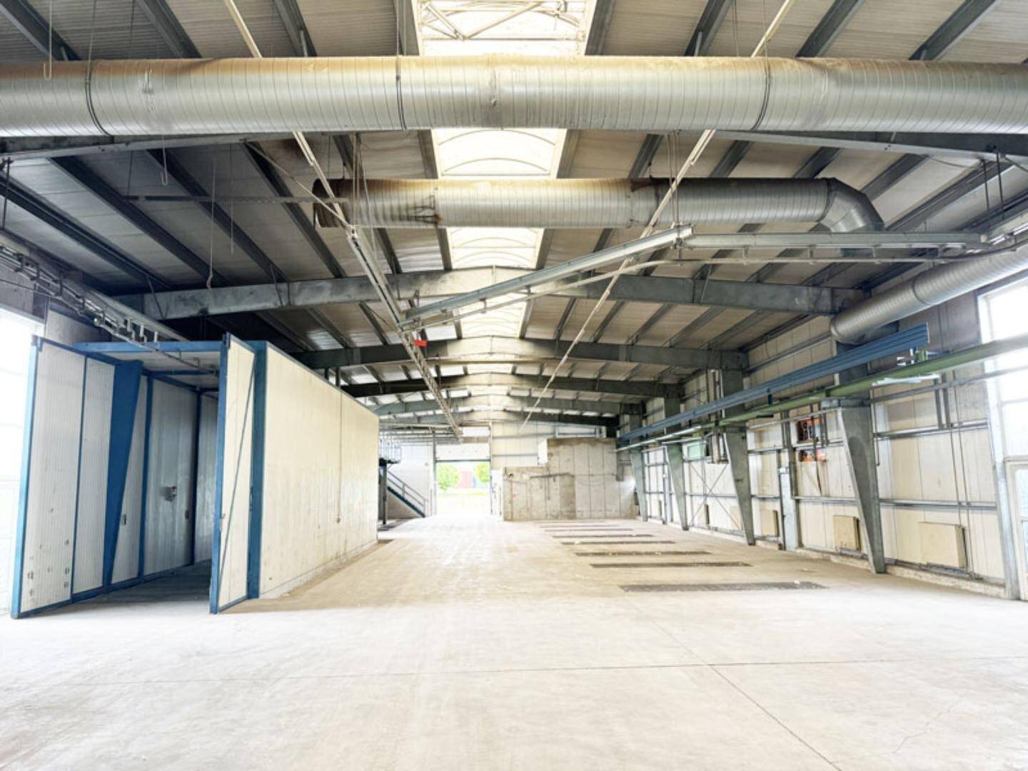 Geräumige Industriehalle mit hohen Decken, sichtbaren Lüftungsrohren und Oberlichtern für Tageslicht.