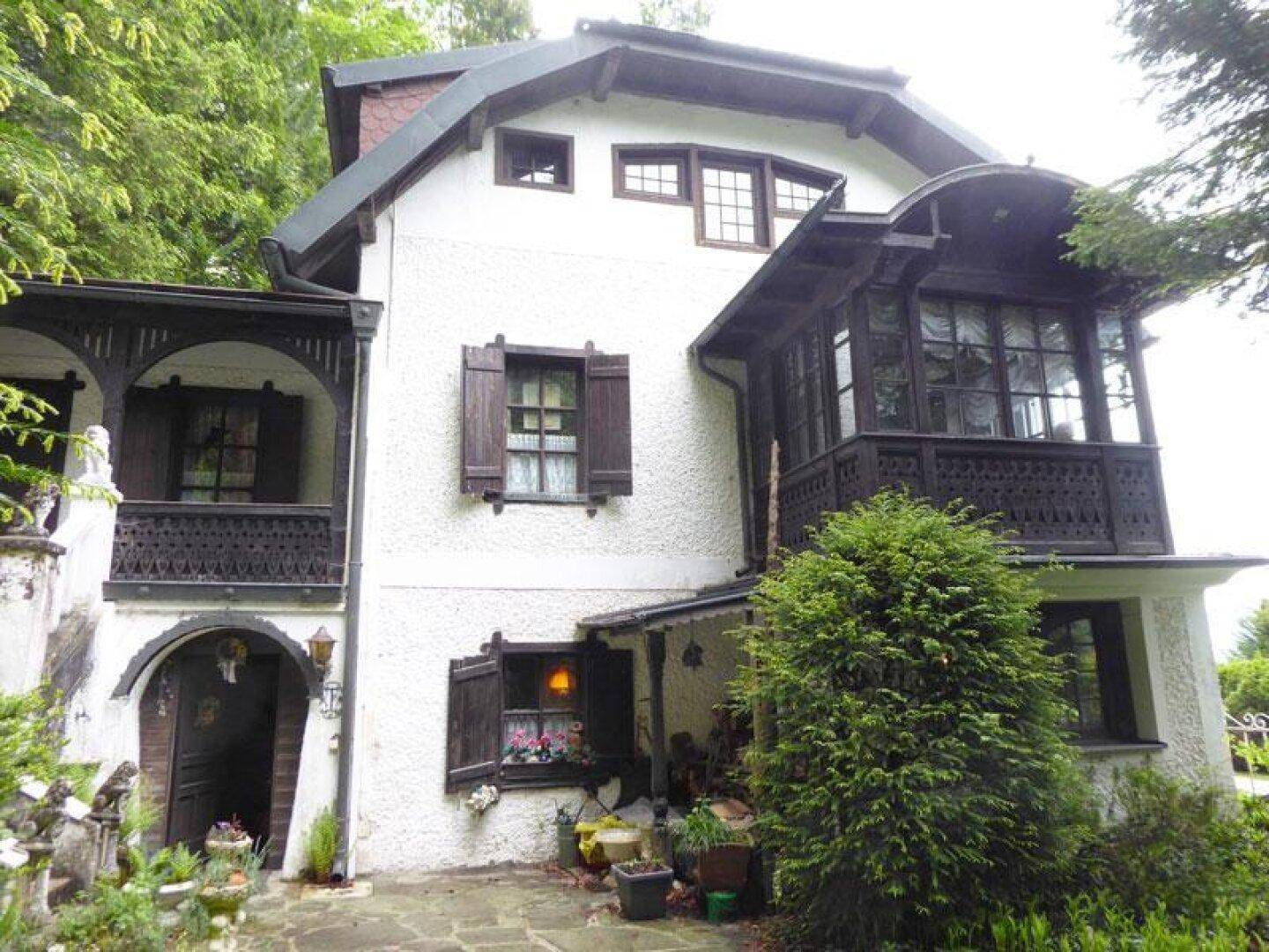 Charmantes traditionelles Haus mit weißer Putzfassade, dunklen Holzdetails und verzierten Balkonen.