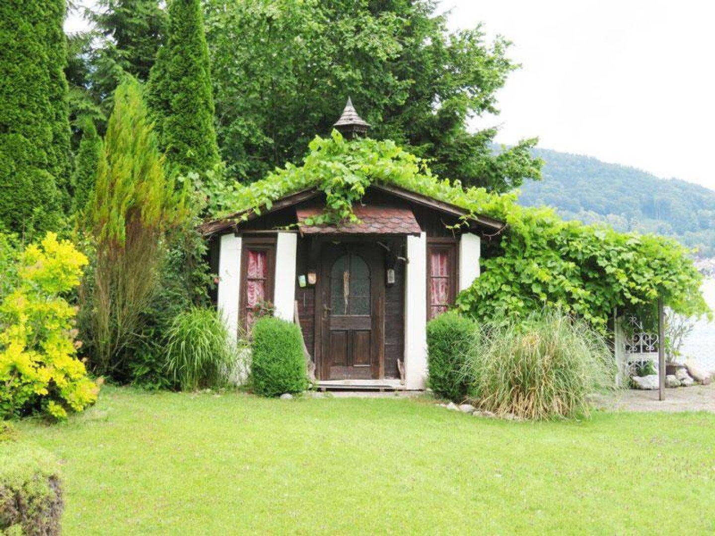 Kleines Gartenhaus umgeben von üppigem Grün und Rasenfläche mit Blick auf die Landschaft.