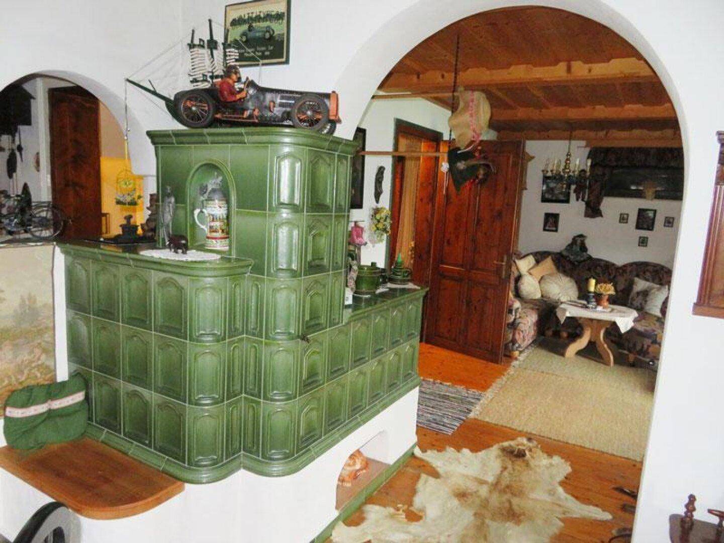 Gemütliches Wohnzimmer mit traditionellem grünem Kachelofen, Holzbalkendecke und rustikalem Charme.