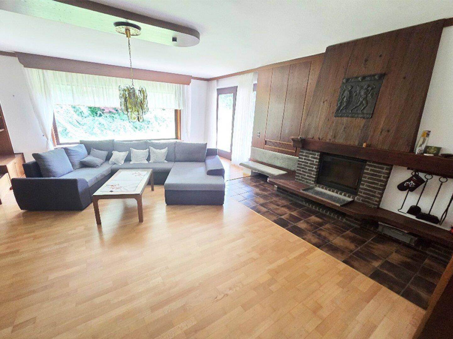 Geräumiges Wohnzimmer mit gemütlichem Kamin, Holzboden und großem Ecksofa, hell durch große Fenster.