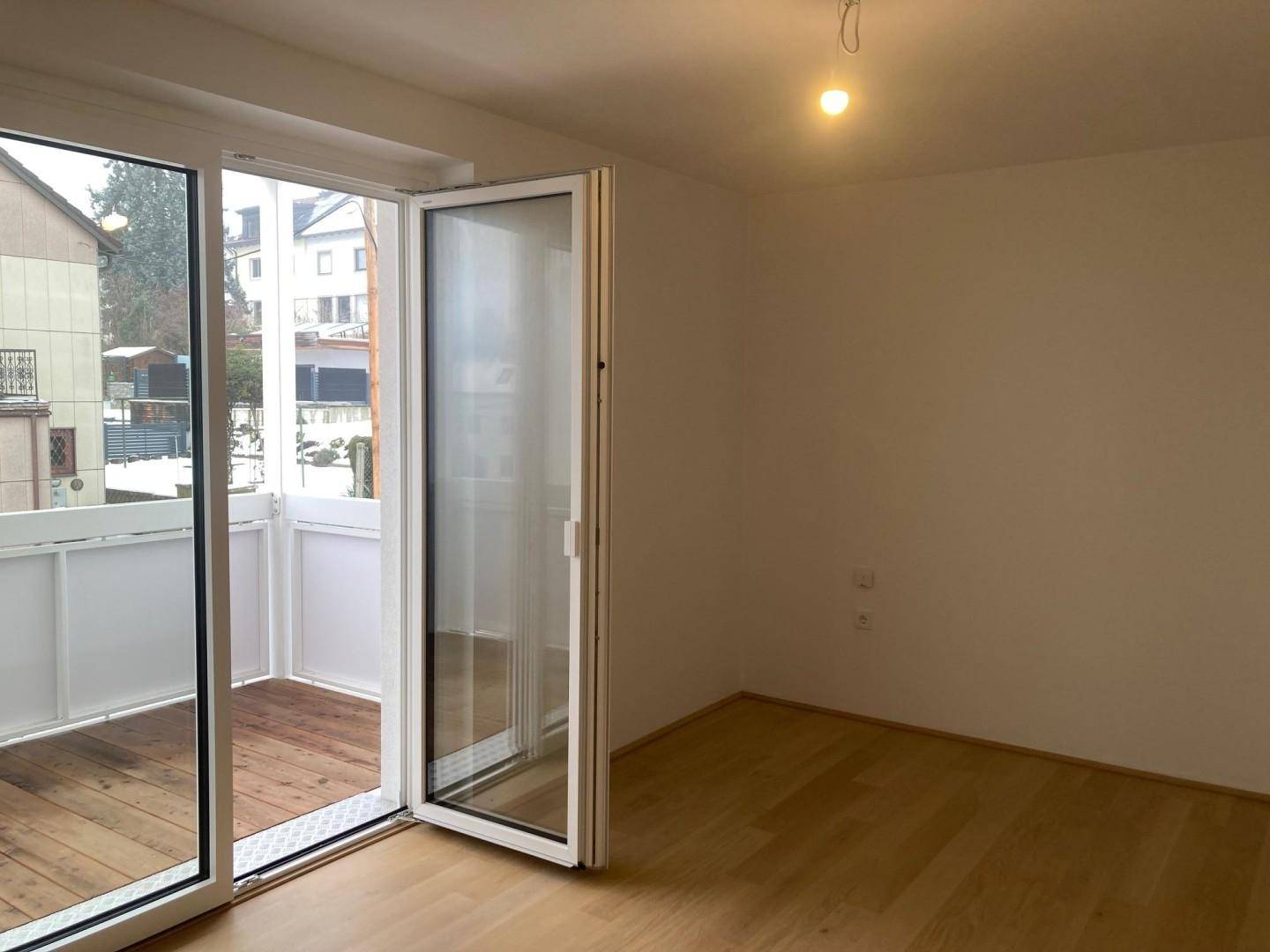 Heller Raum mit Zugang zu einem verglasten Balkon mit Holzboden.