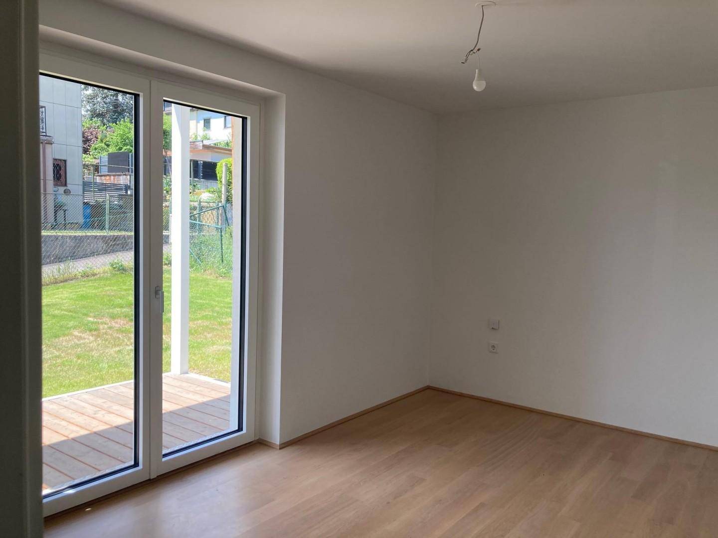 Heller Raum mit Holzboden und großen Glastüren, die Zugang zu einer Terrasse und dem Garten bieten.