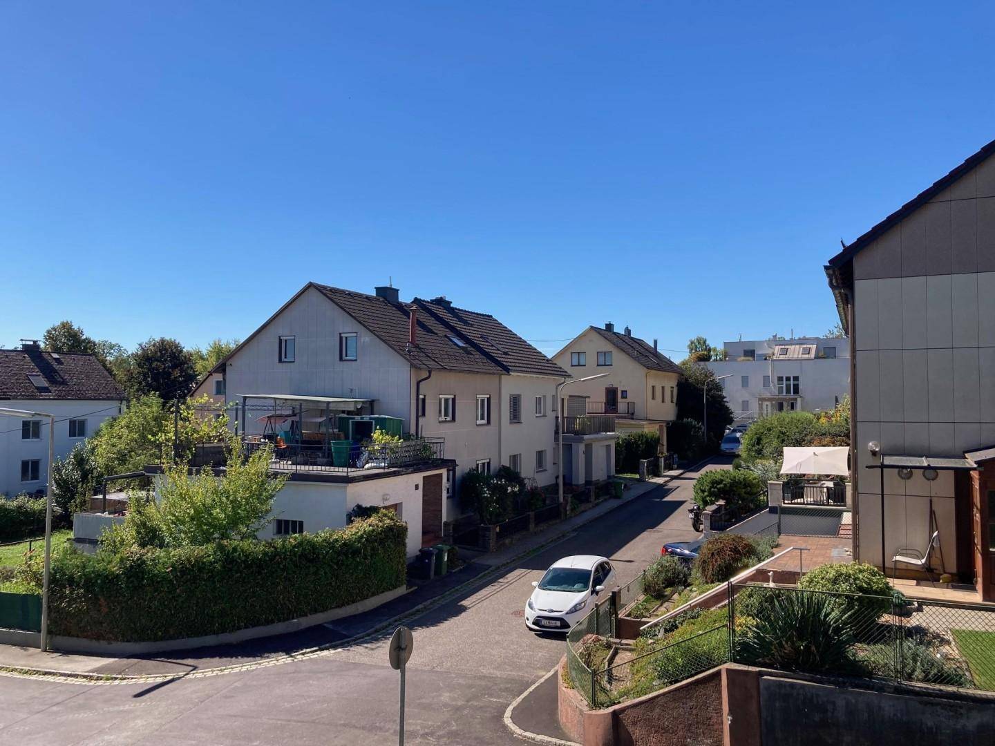 Blick auf eine ruhige Wohnstraße mit gepflegten Häusern und parkenden Autos an einem sonnigen Tag.