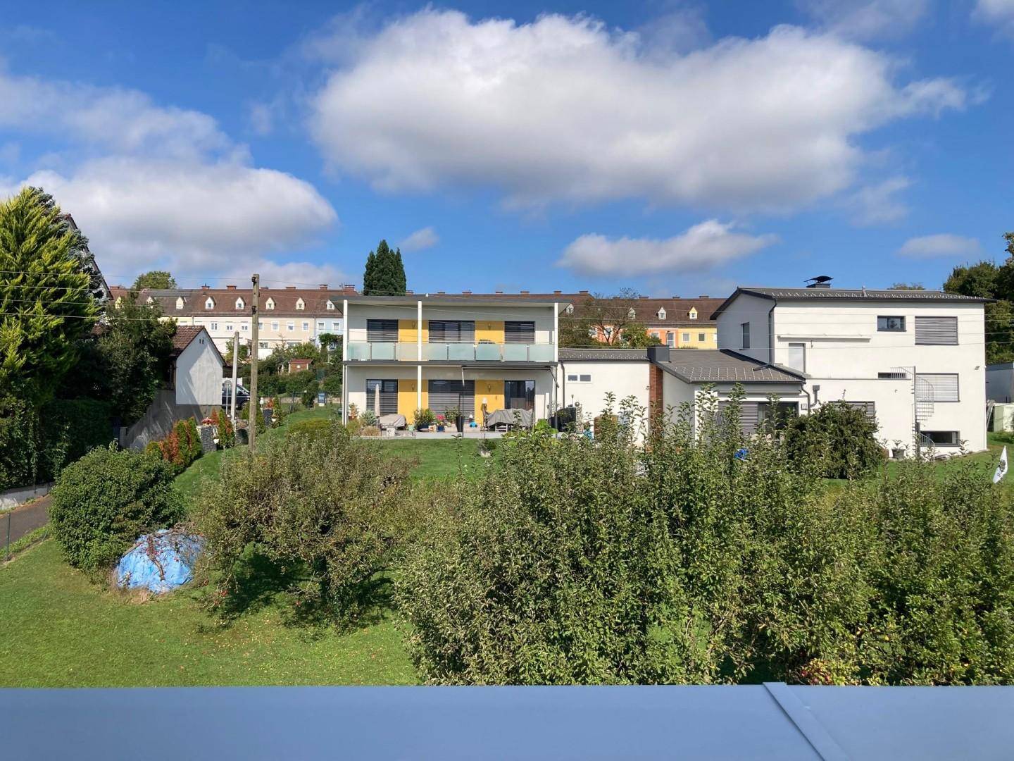 Panoramablick auf eine Wohnsiedlung mit verschiedenen Häusern und üppiger grüner Landschaft unter blauem Himmel.