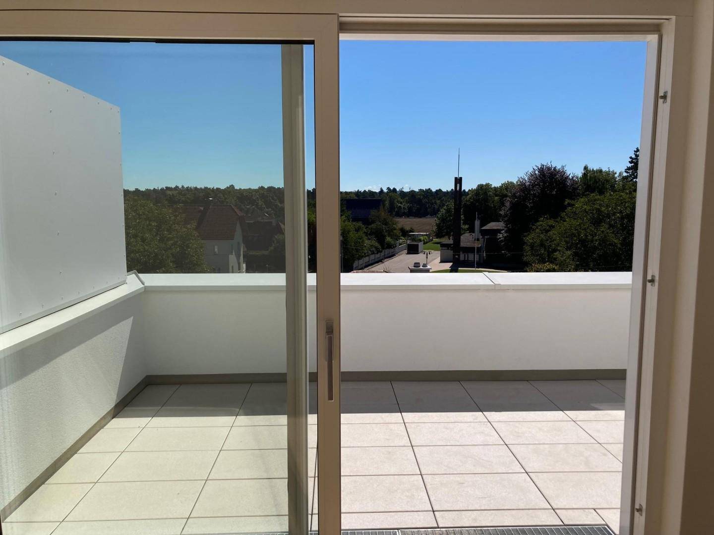 Heller Innenraum mit Schiebetür, die Zugang zu einer großen gefliesten Terrasse mit Weitblick bietet.